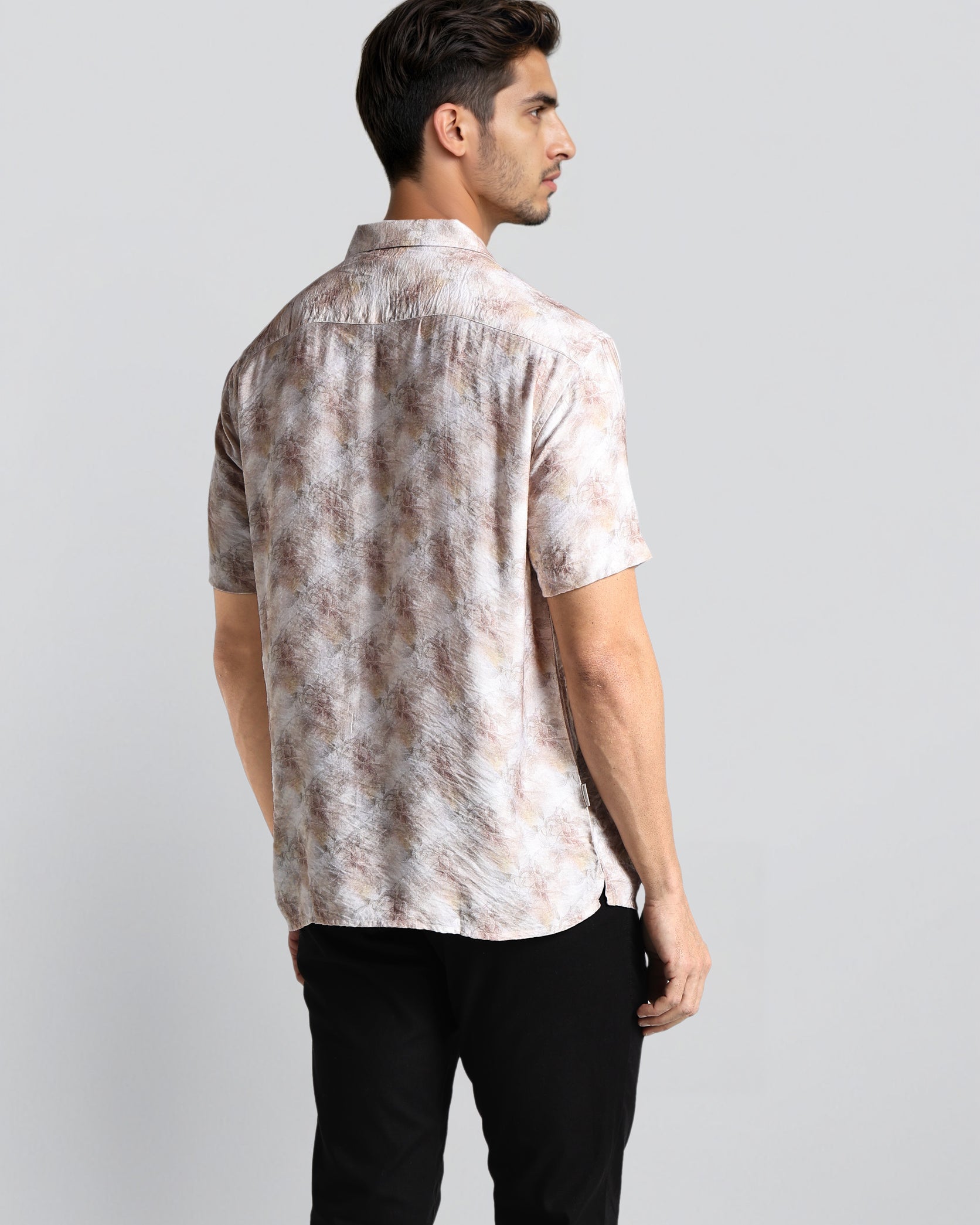 Man wearing a patterned shirt and black pants on a light gray background