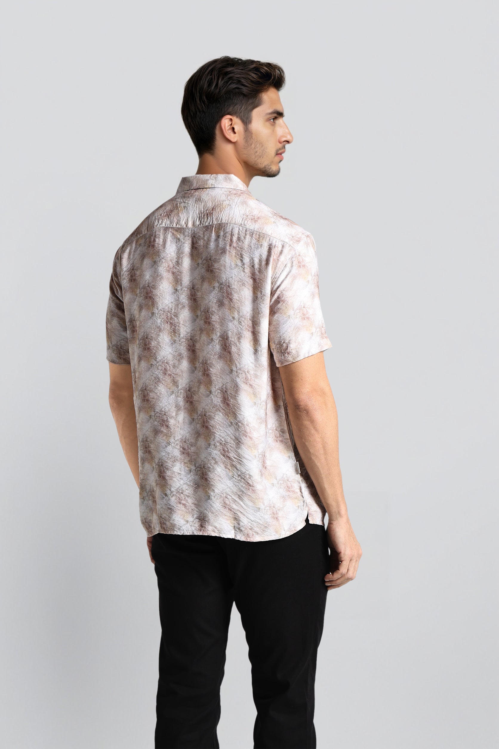 Man wearing a patterned shirt and black pants on a light gray background