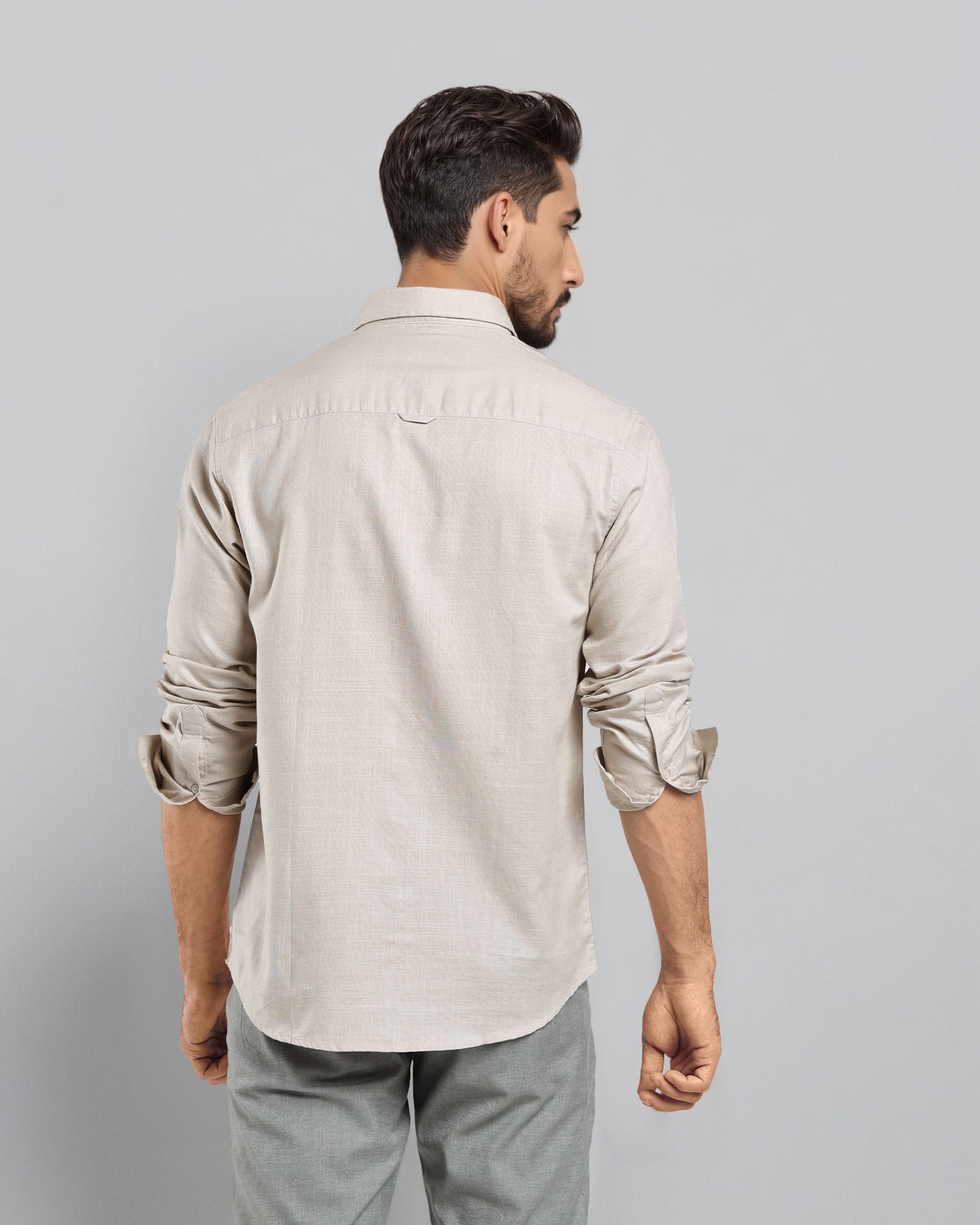 Man wearing a beige shirt and gray pants against a light gray background