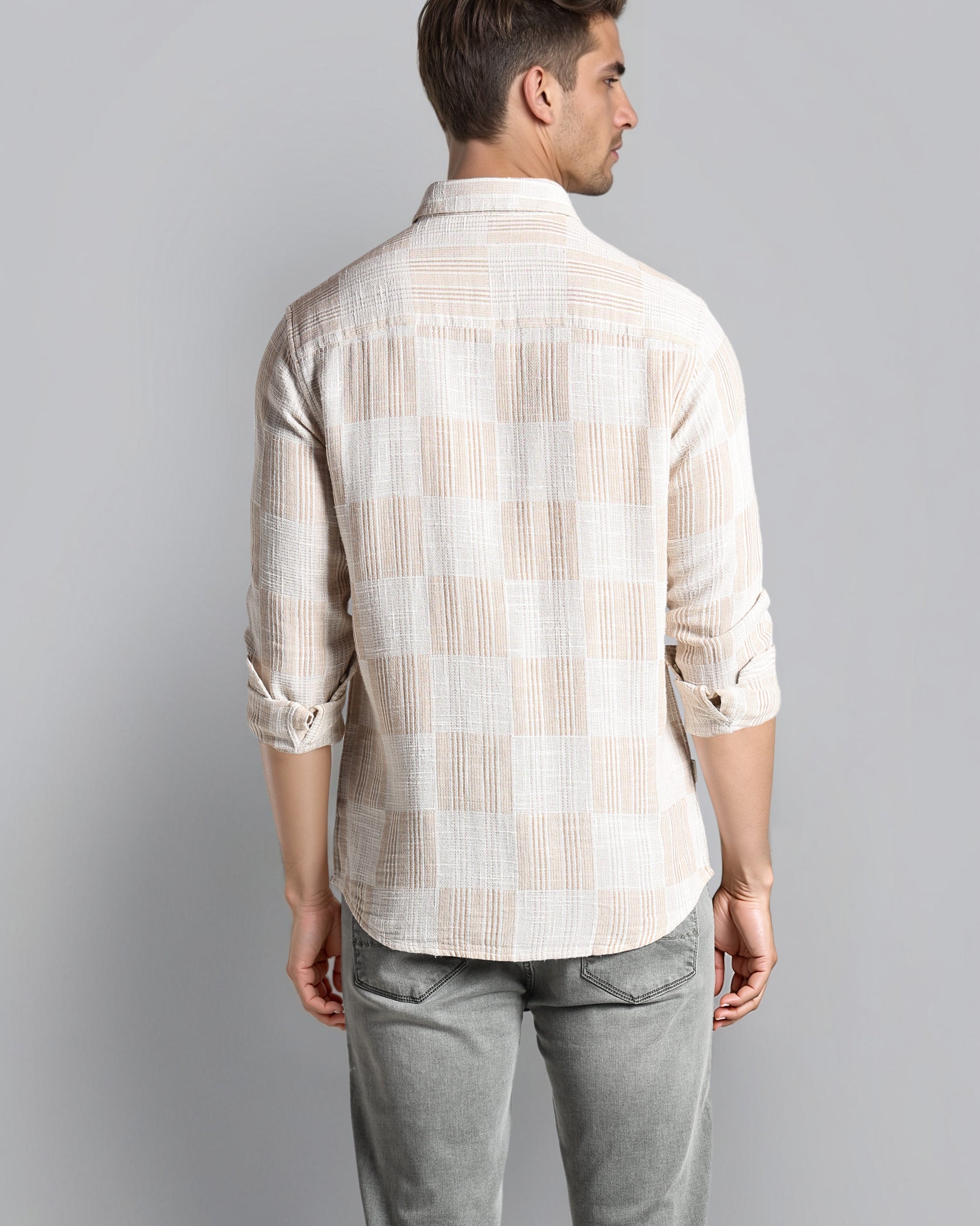 Man wearing a checkered shirt and gray pants against a plain background