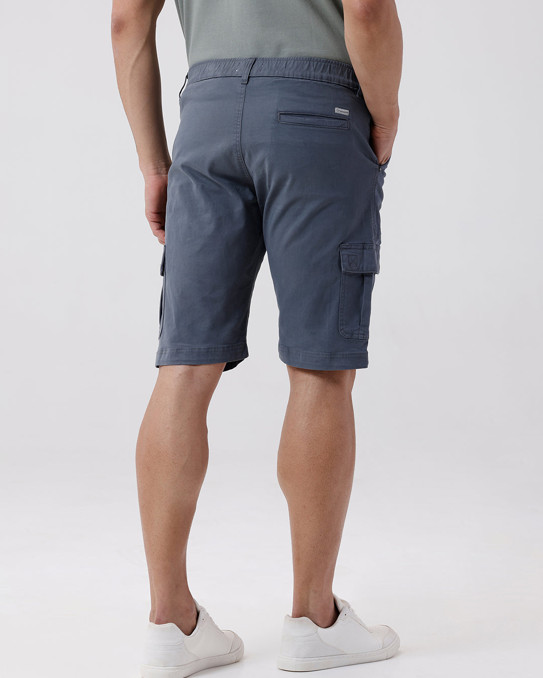 Man wearing a grey garment dyed cargo shorts in dark grey with casual styling on a gray background