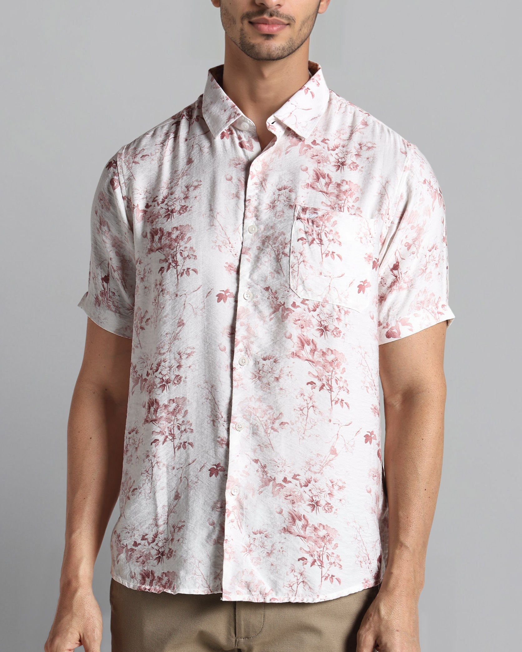 Man wearing a white shirt with red floral pattern on a gray background