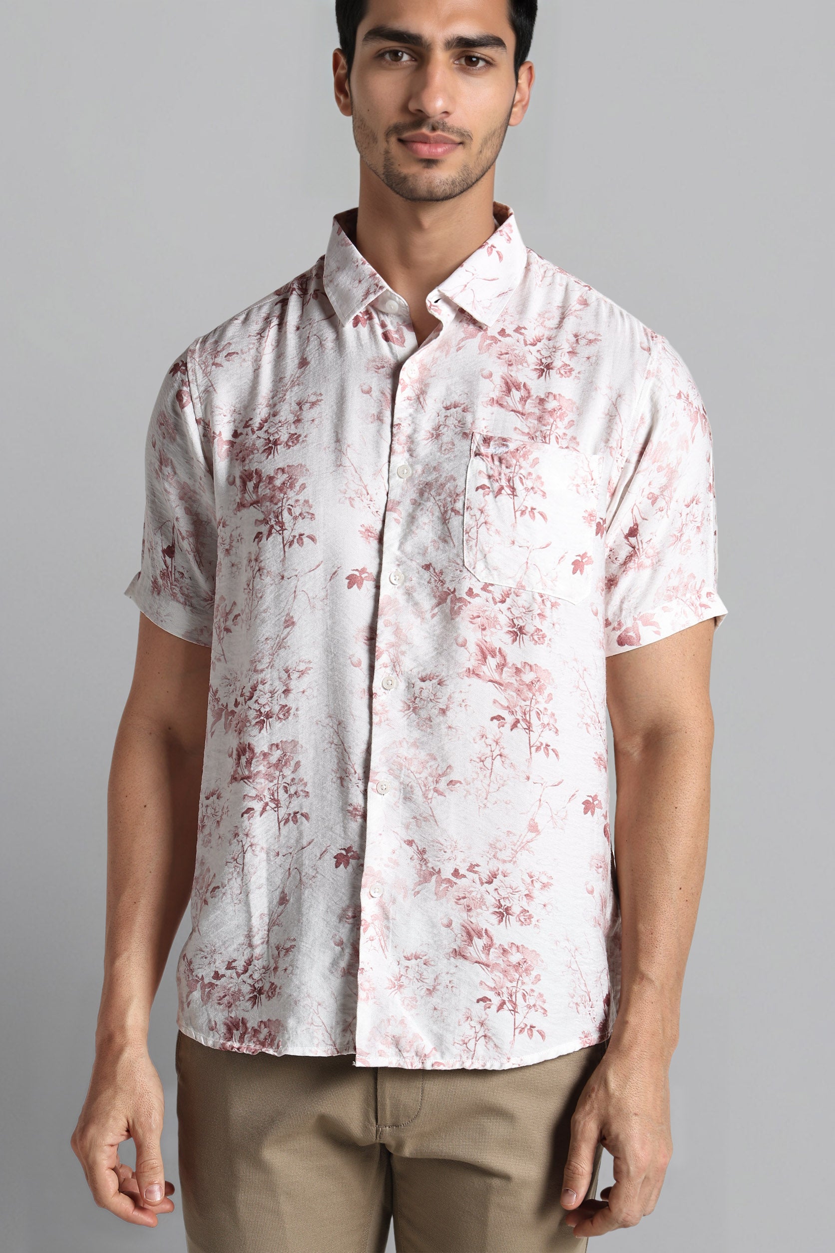 Man wearing a white shirt with red floral pattern on a gray background