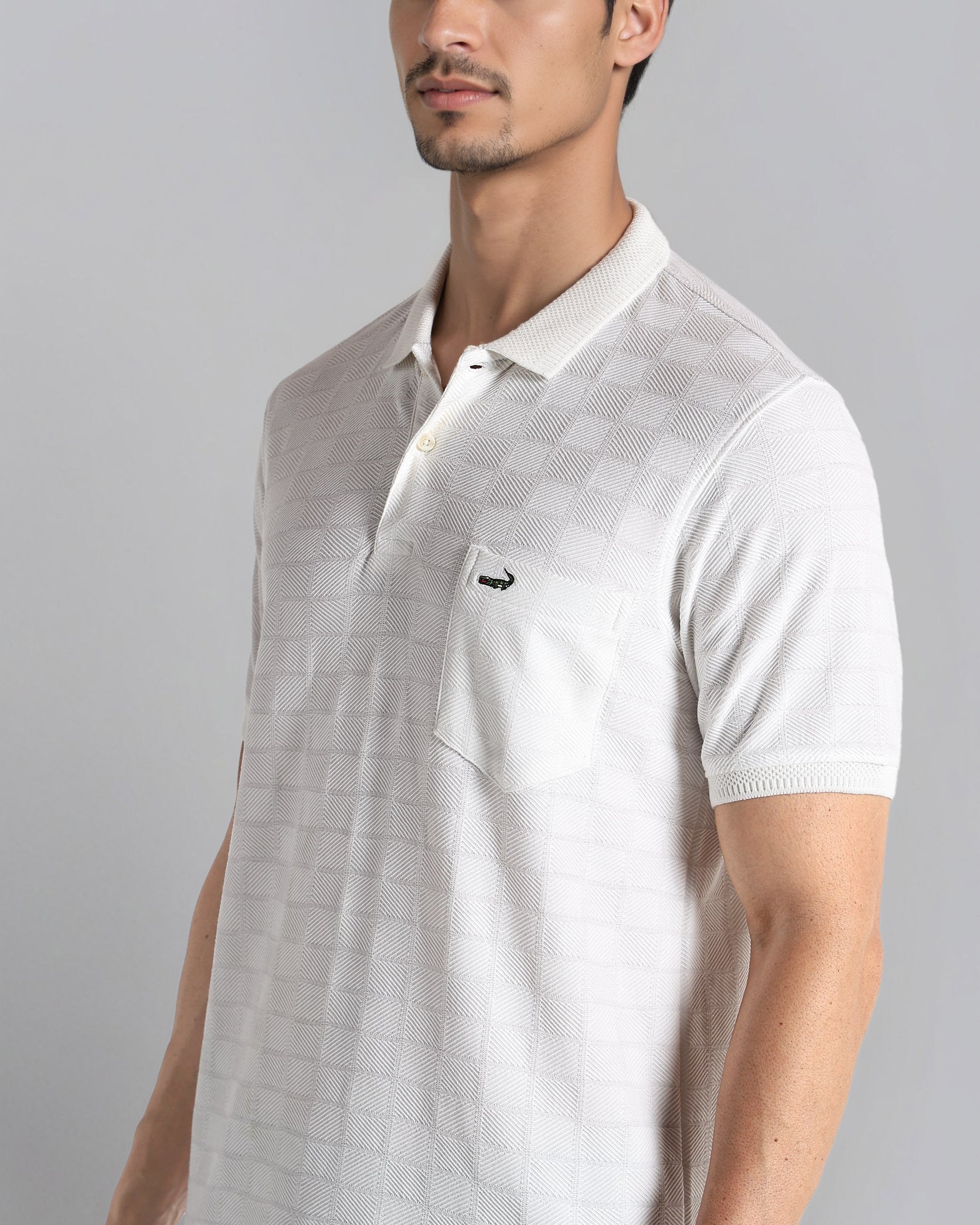 Man wearing a white polo shirt with a small logo on a gray background