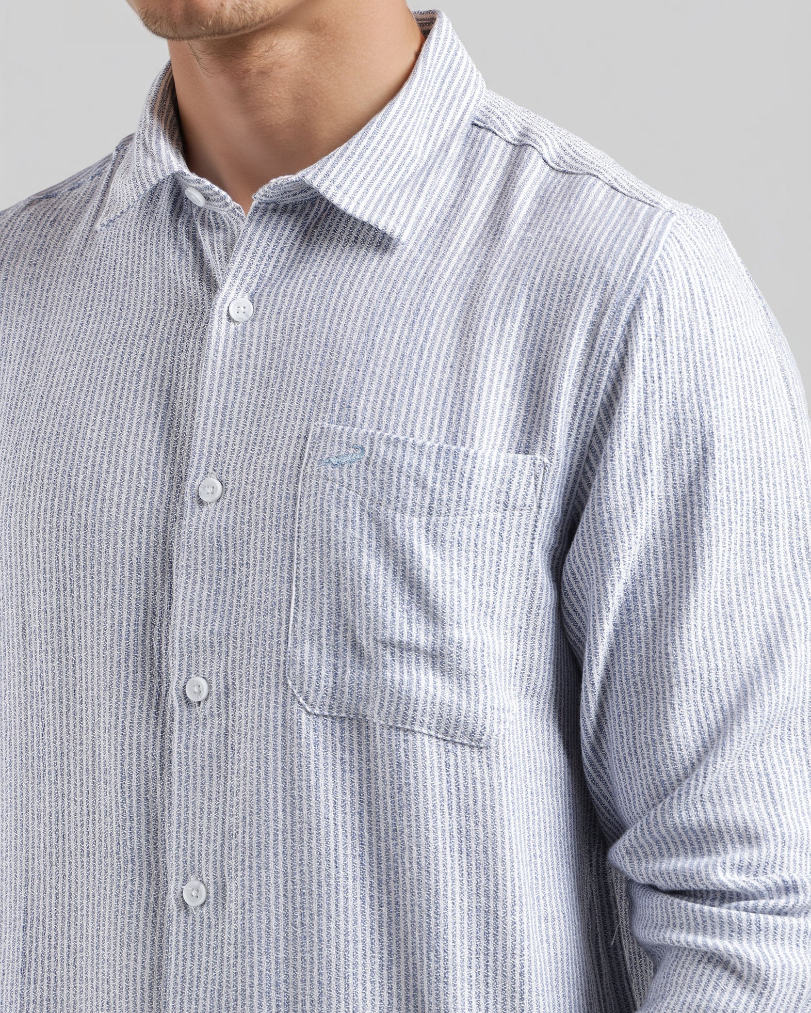 Close-up of a person wearing a light blue and white striped shirt with a pocket on a gray background