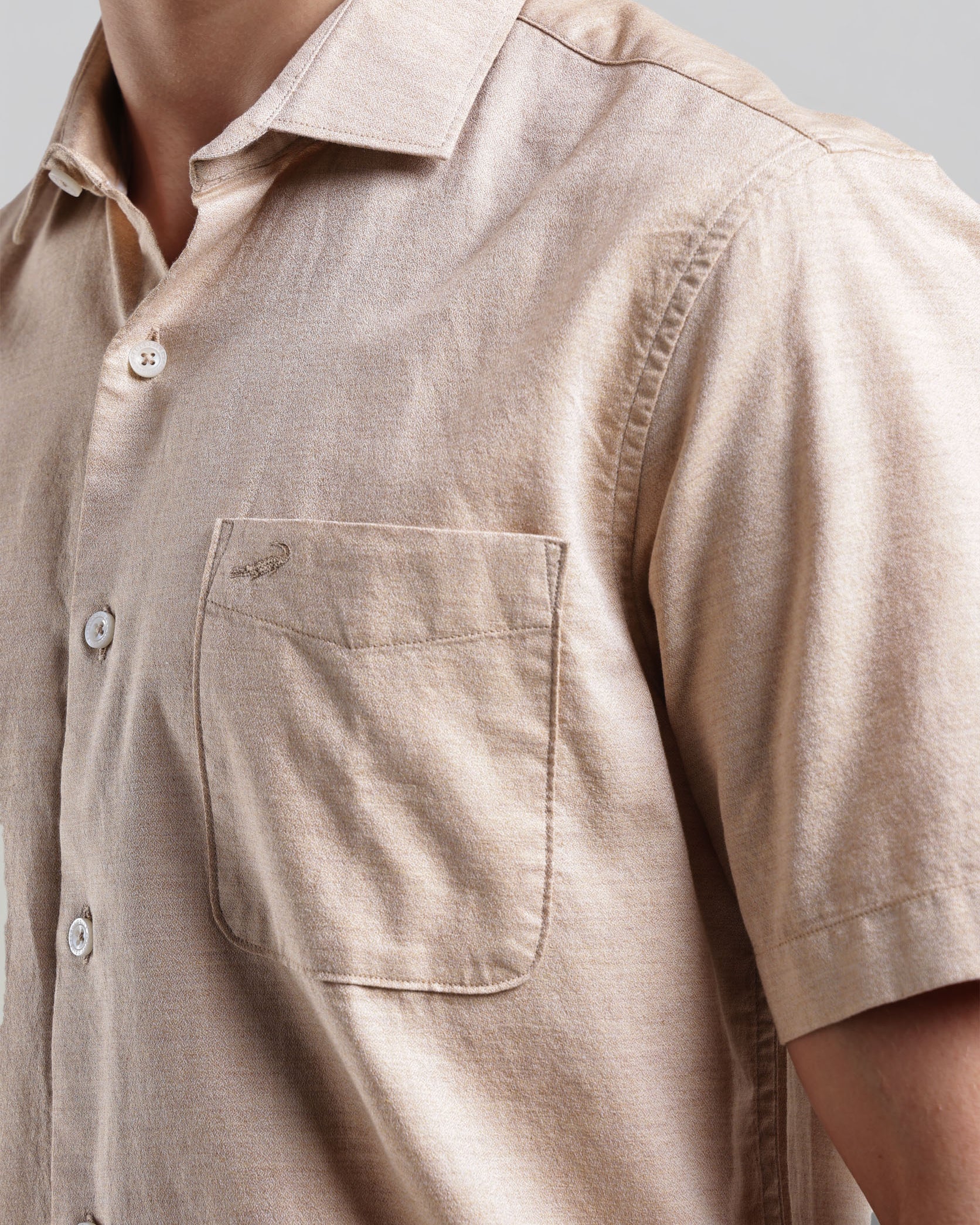 Close-up of a beige short-sleeve shirt with a pocket on a neutral background