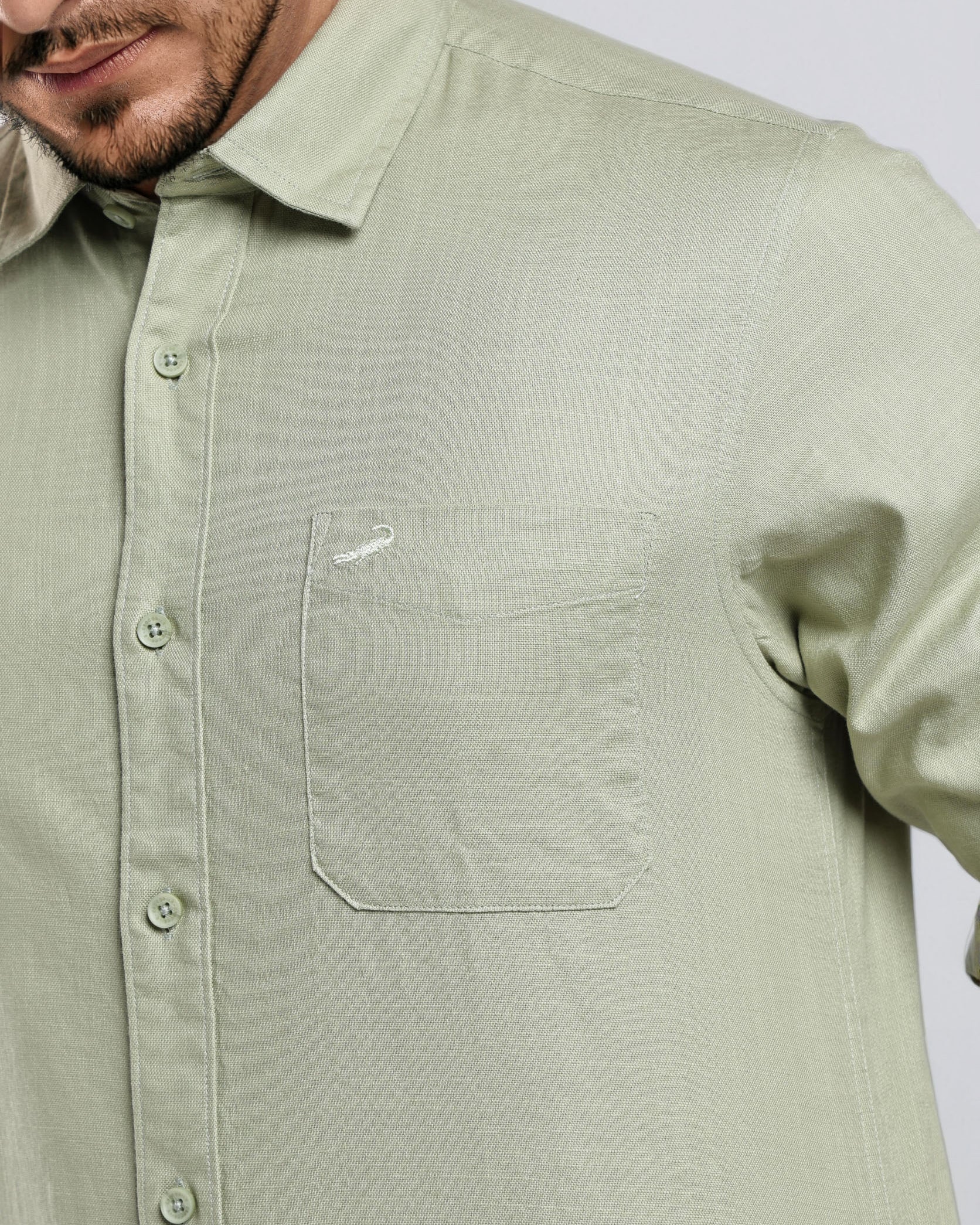 Man wearing a light green button-up shirt with a small logo on a white background