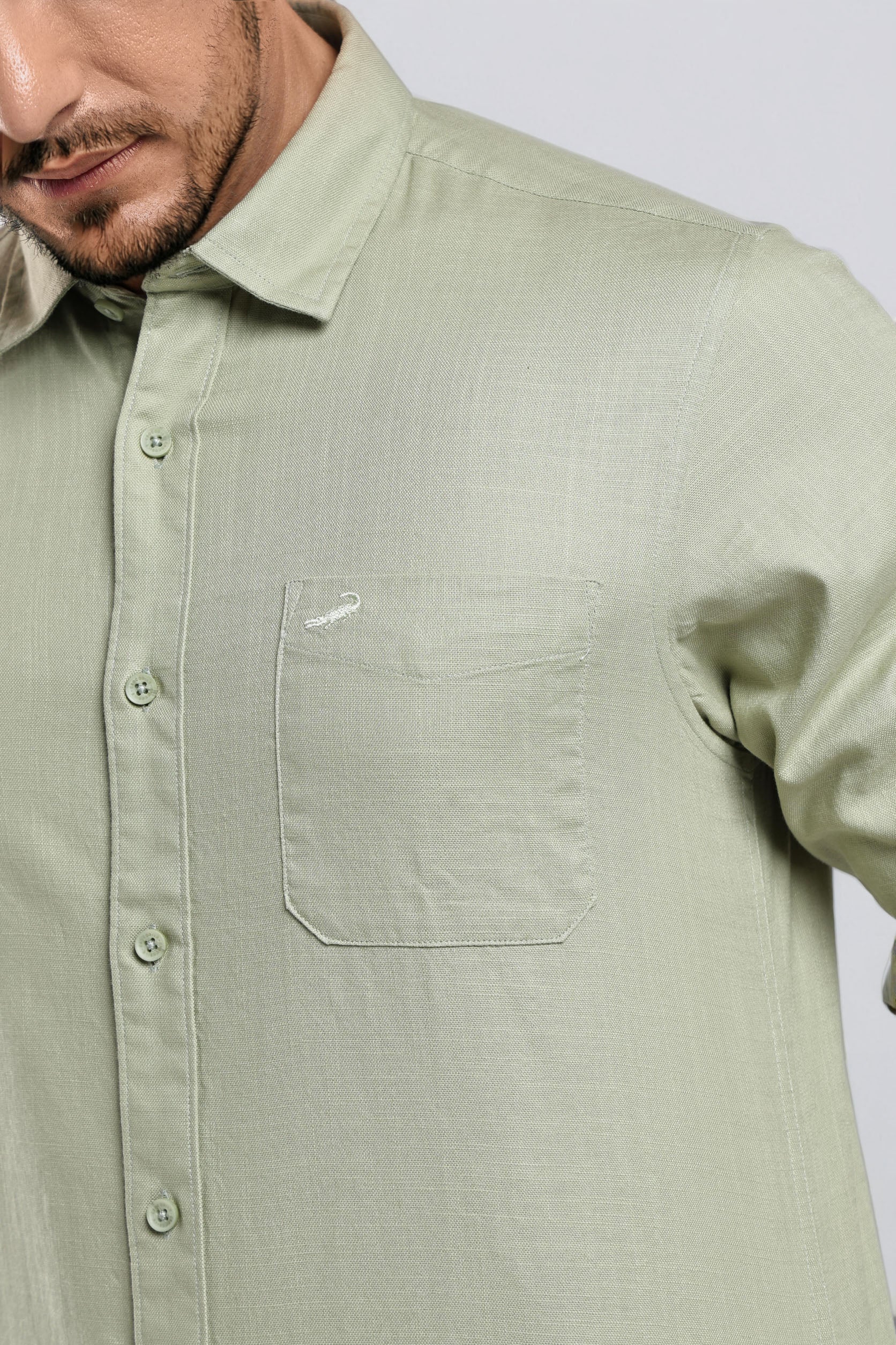 Man wearing a light green button-up shirt with a small logo on a white background