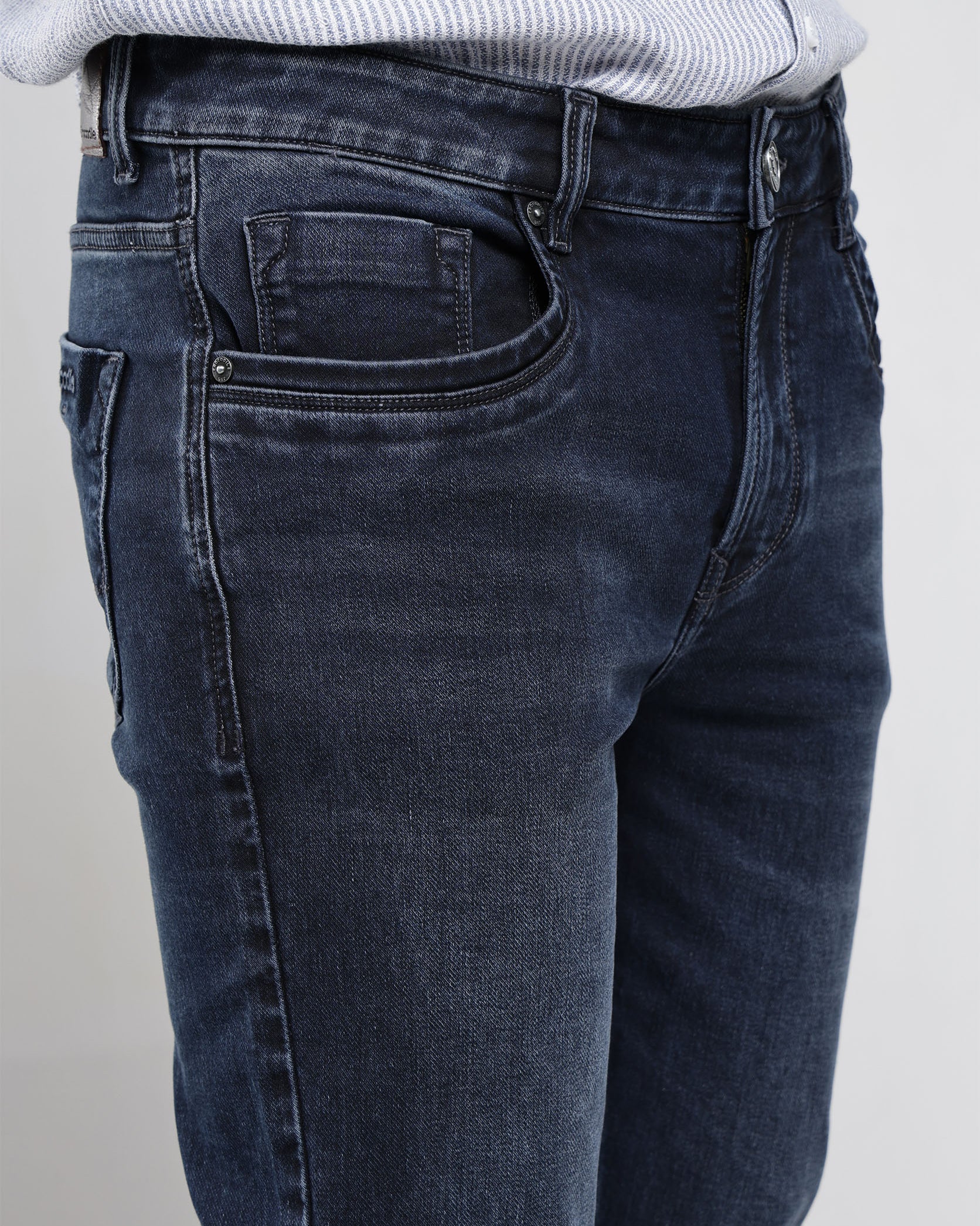 Dark blue jeans worn by a person on a plain background