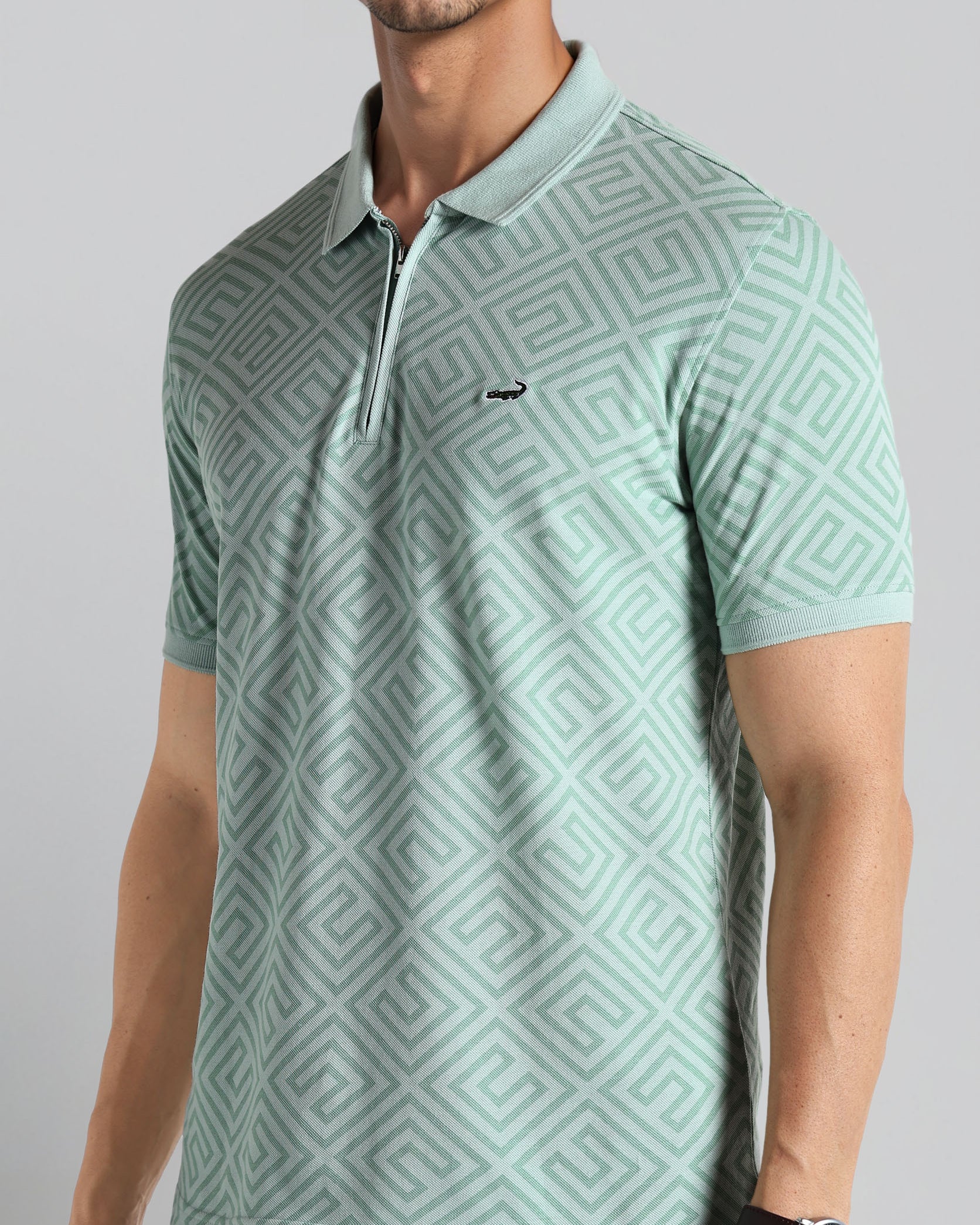 Man wearing a light green patterned polo shirt on a gray background
