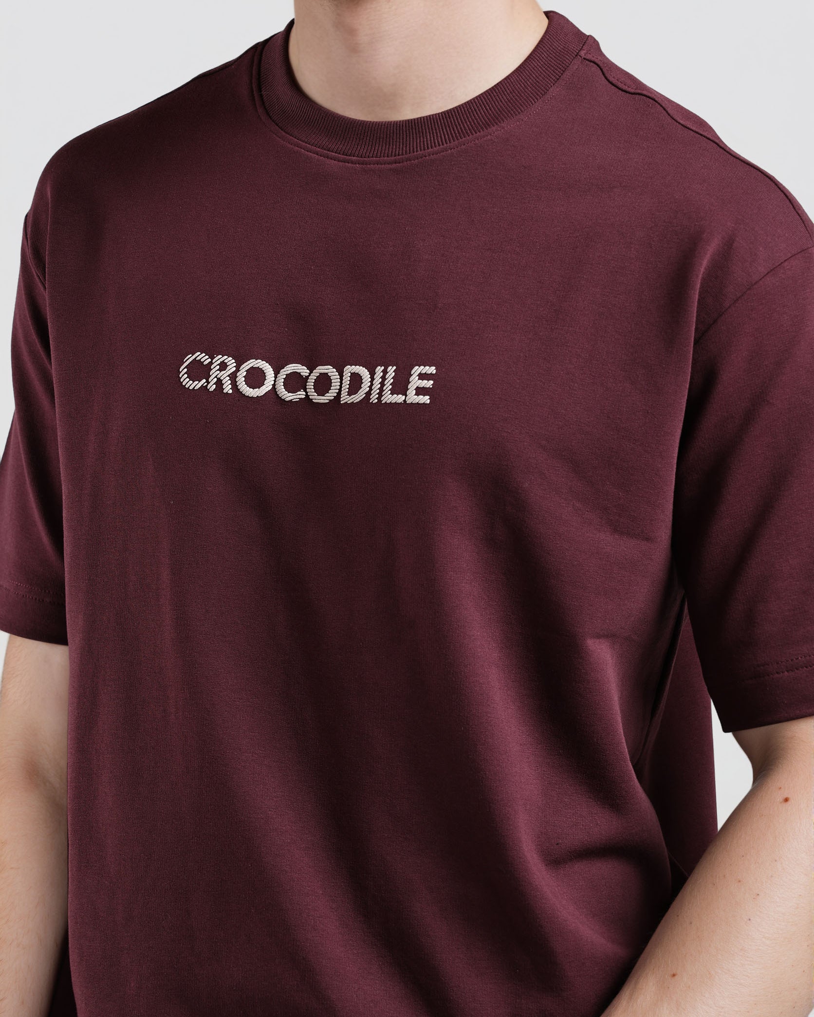 Maroon t-shirt with 'CROCODILE' logo worn by a person on a light gray background
