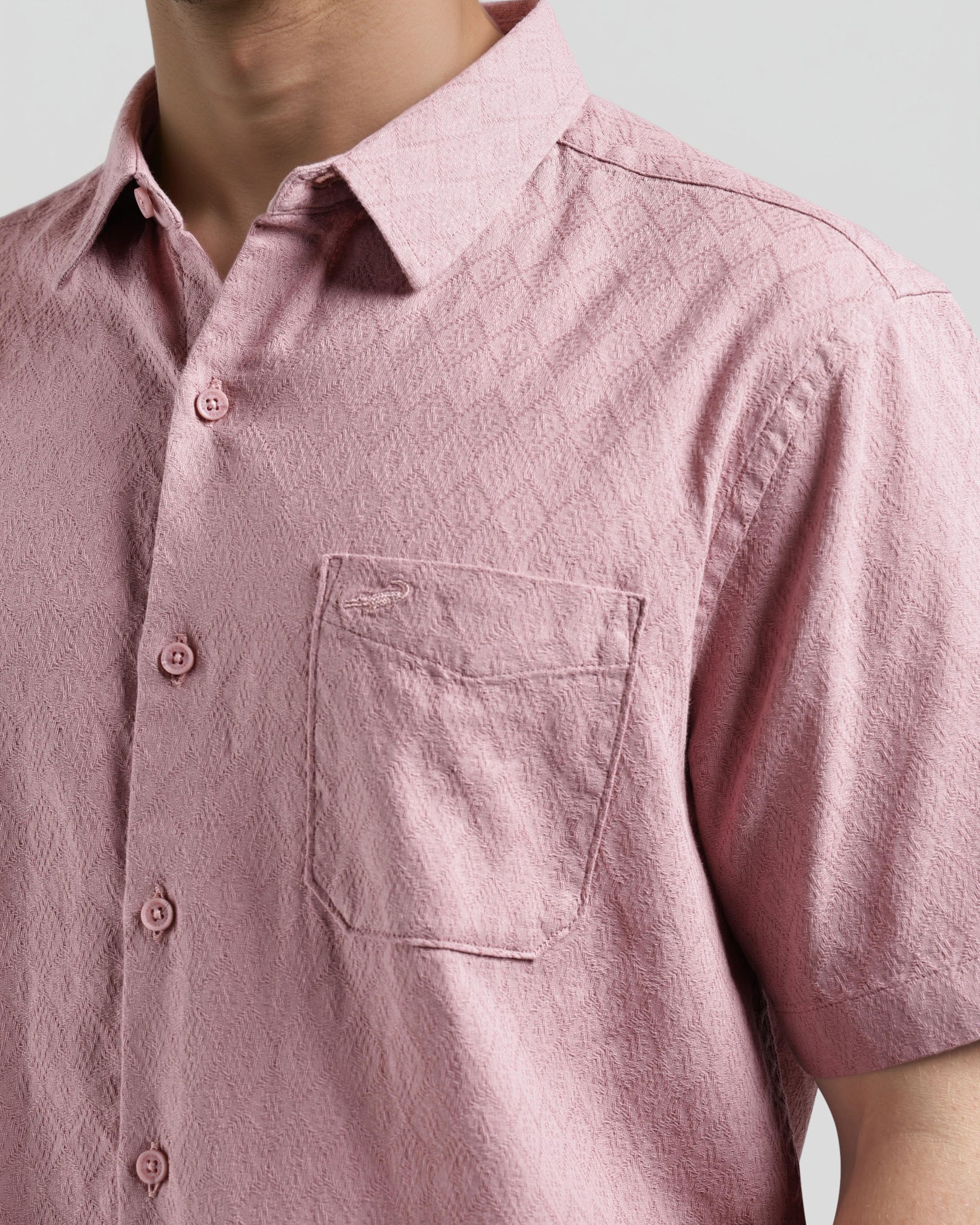 Close-up of a person wearing a pink short-sleeve shirt with a pocket on a light gray background