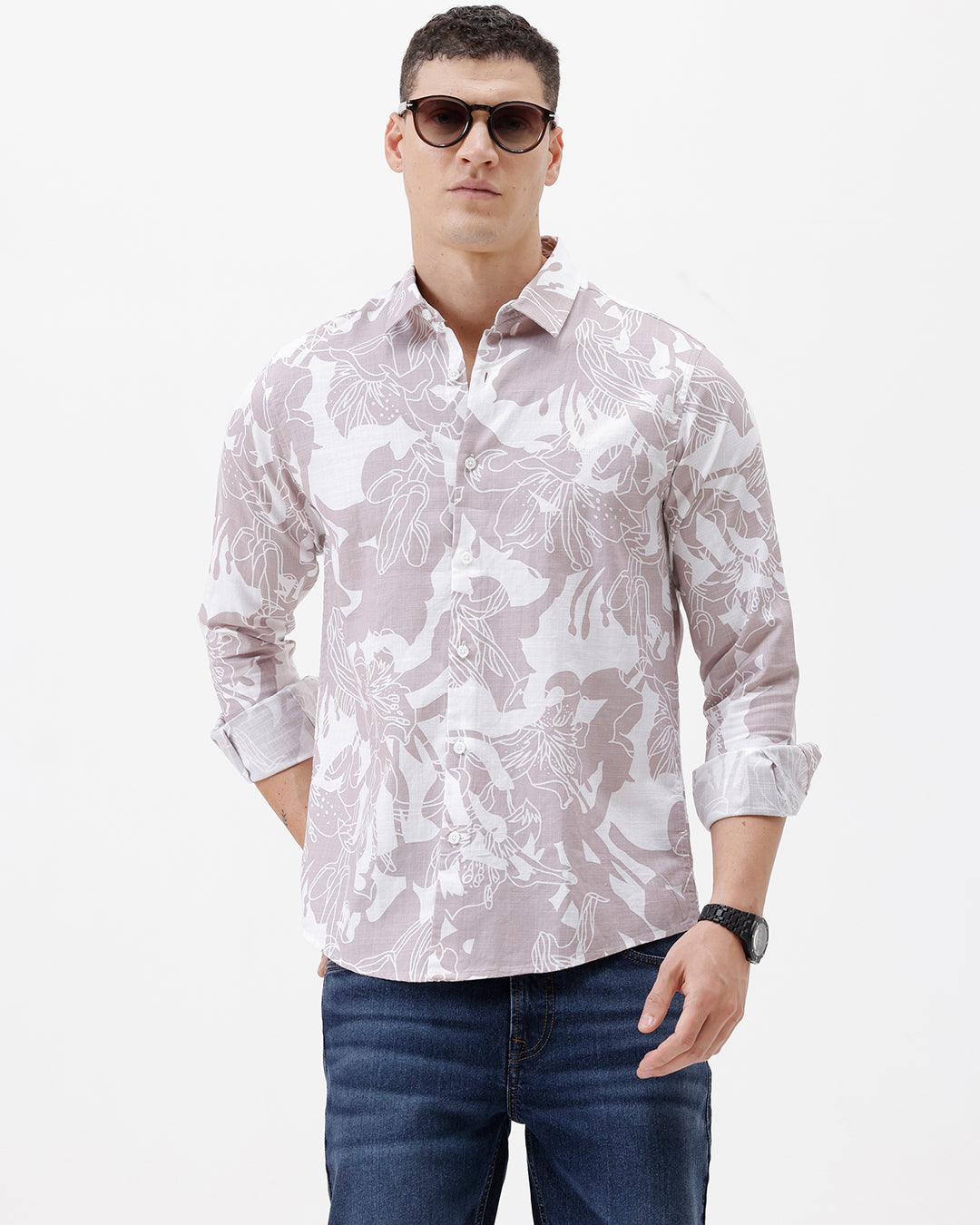A man wearing a long-sleeve button-up shirt with a light gray and white abstract floral pattern, paired with dark blue jeans, standing against a plain white background.