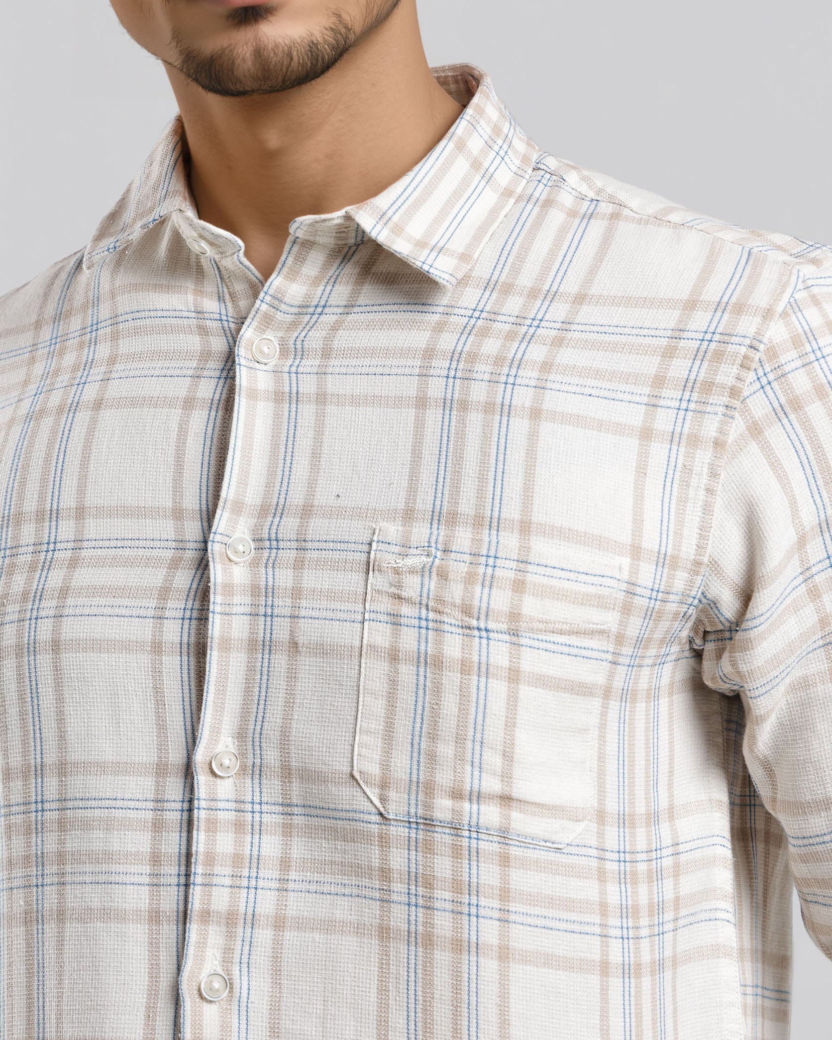 Man wearing a beige and blue plaid shirt against a gray background