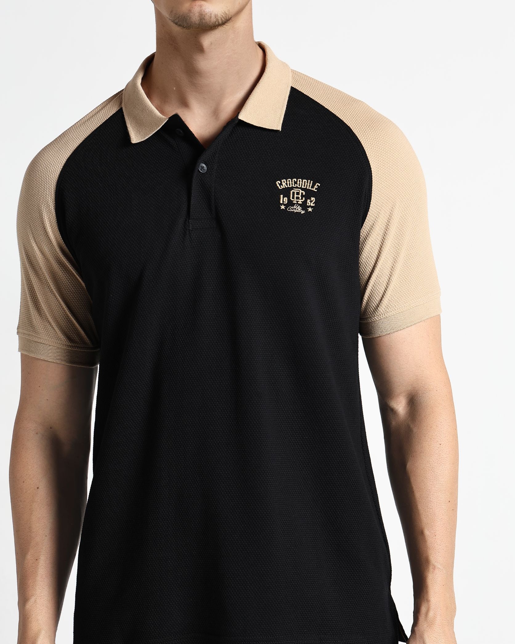 Man wearing a black and beige polo shirt with a logo on a white background