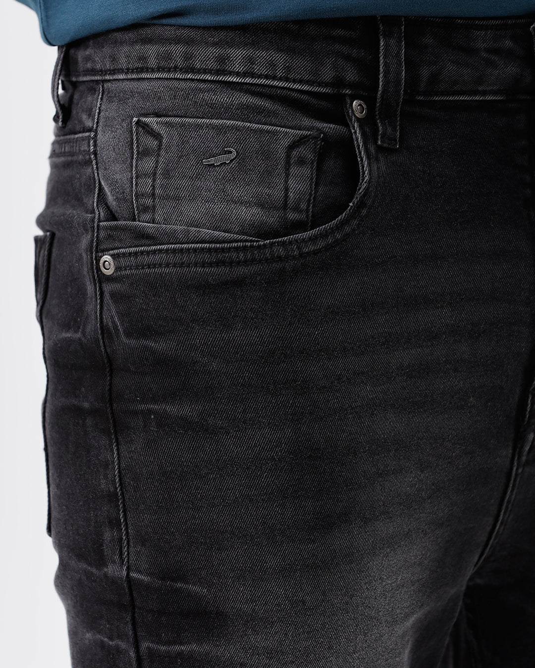A person wearing slim-fit black denim jeans with a faded wash, paired with a dark blue t-shirt and black leather boots, shown from the waist down on a light gray studio background.
