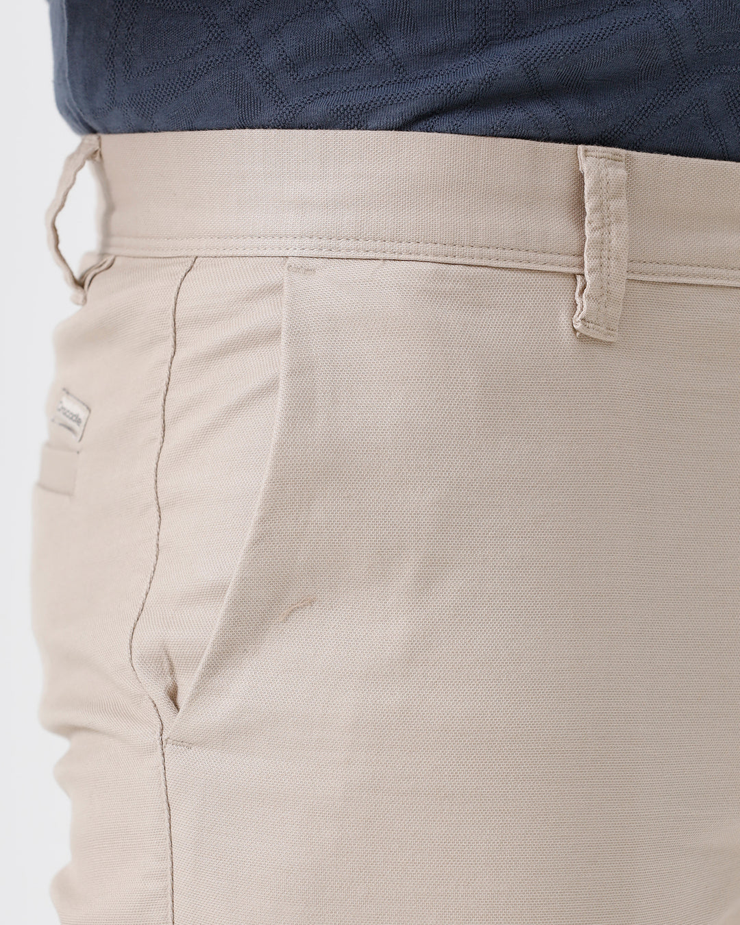 A person wearing slim-fit beige chinos with a blue patterned t-shirt and white sneakers, standing against a white studio background.