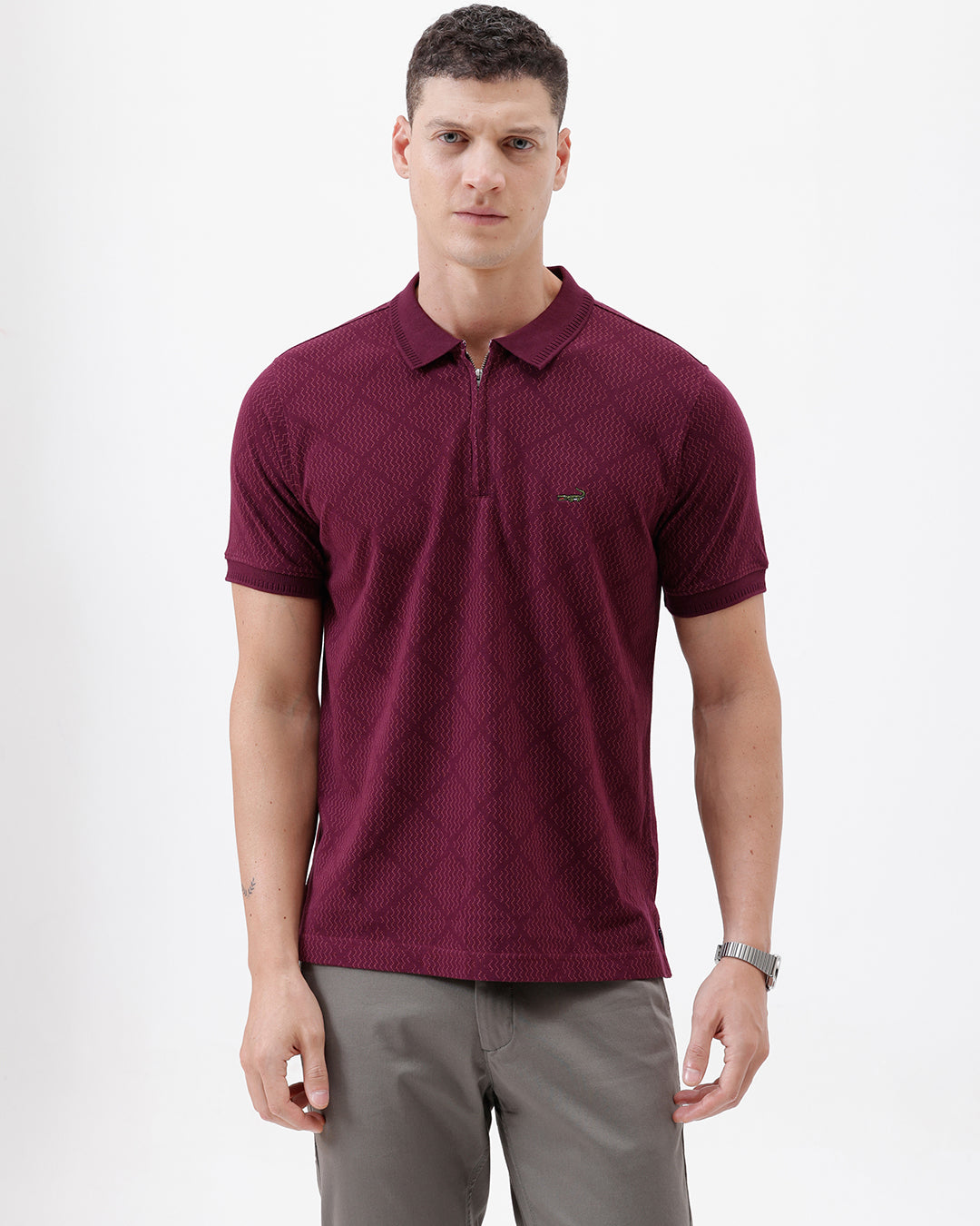 A man wearing a short-sleeve polo shirt in deep burgundy with a subtle textured geometric pattern, styled with gray trousers, sunglasses, and a watch against a plain white background.