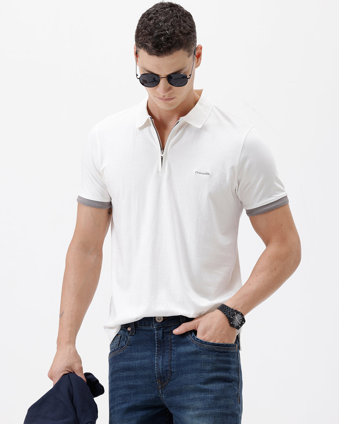 A man wearing a white short-sleeve polo shirt with gray ribbed trim on the collar and sleeve cuffs, paired with dark blue jeans, photographed against a plain white studio background.