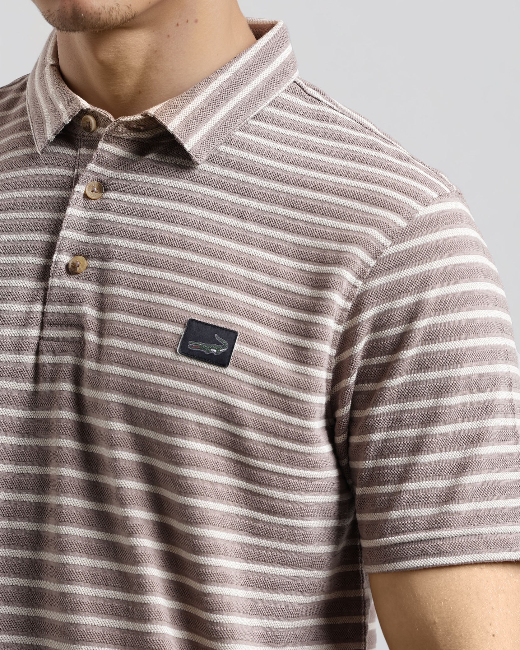Close-up of a person wearing a striped polo shirt with a brand logo on a plain background