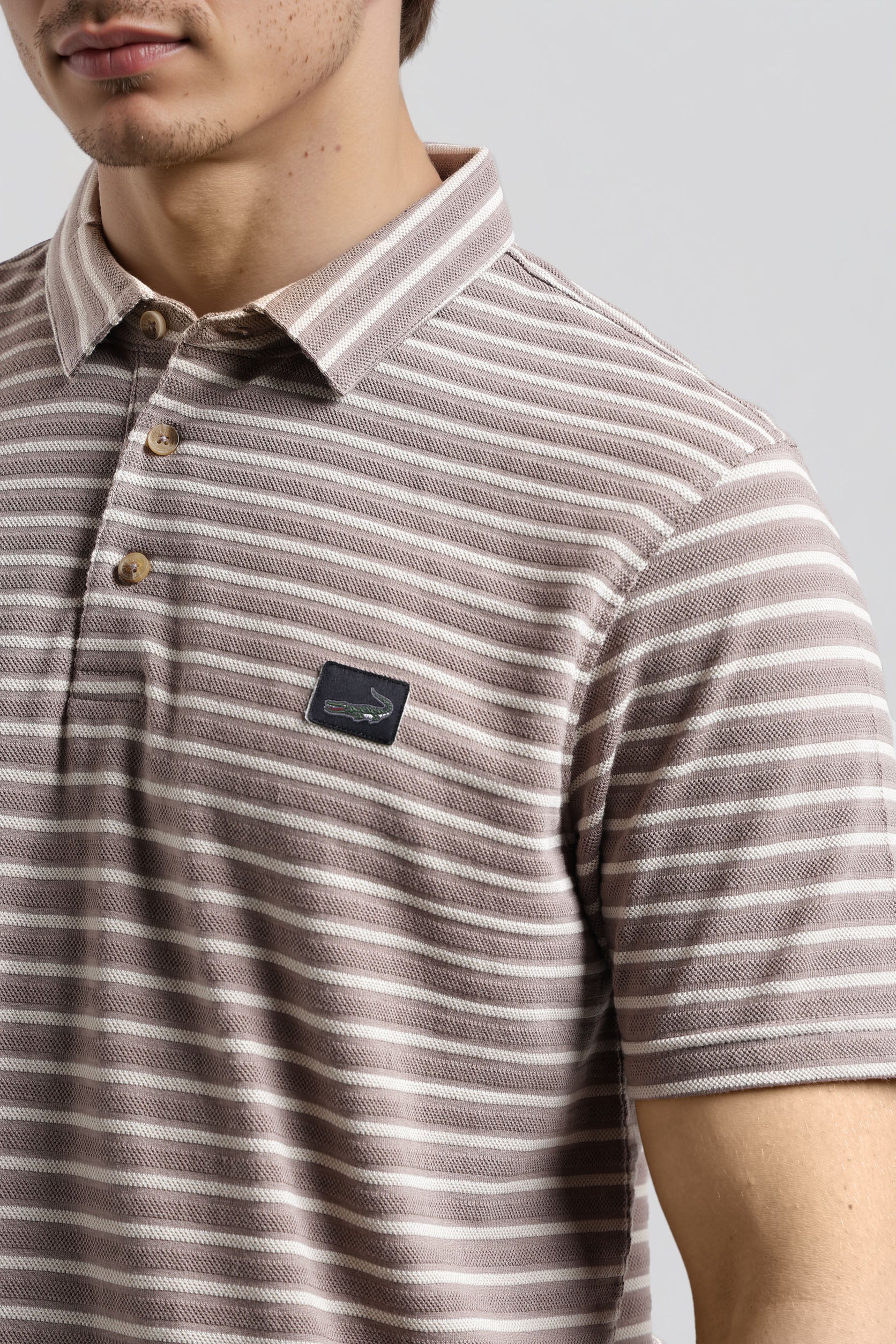 Close-up of a person wearing a striped polo shirt with a brand logo on a plain background
