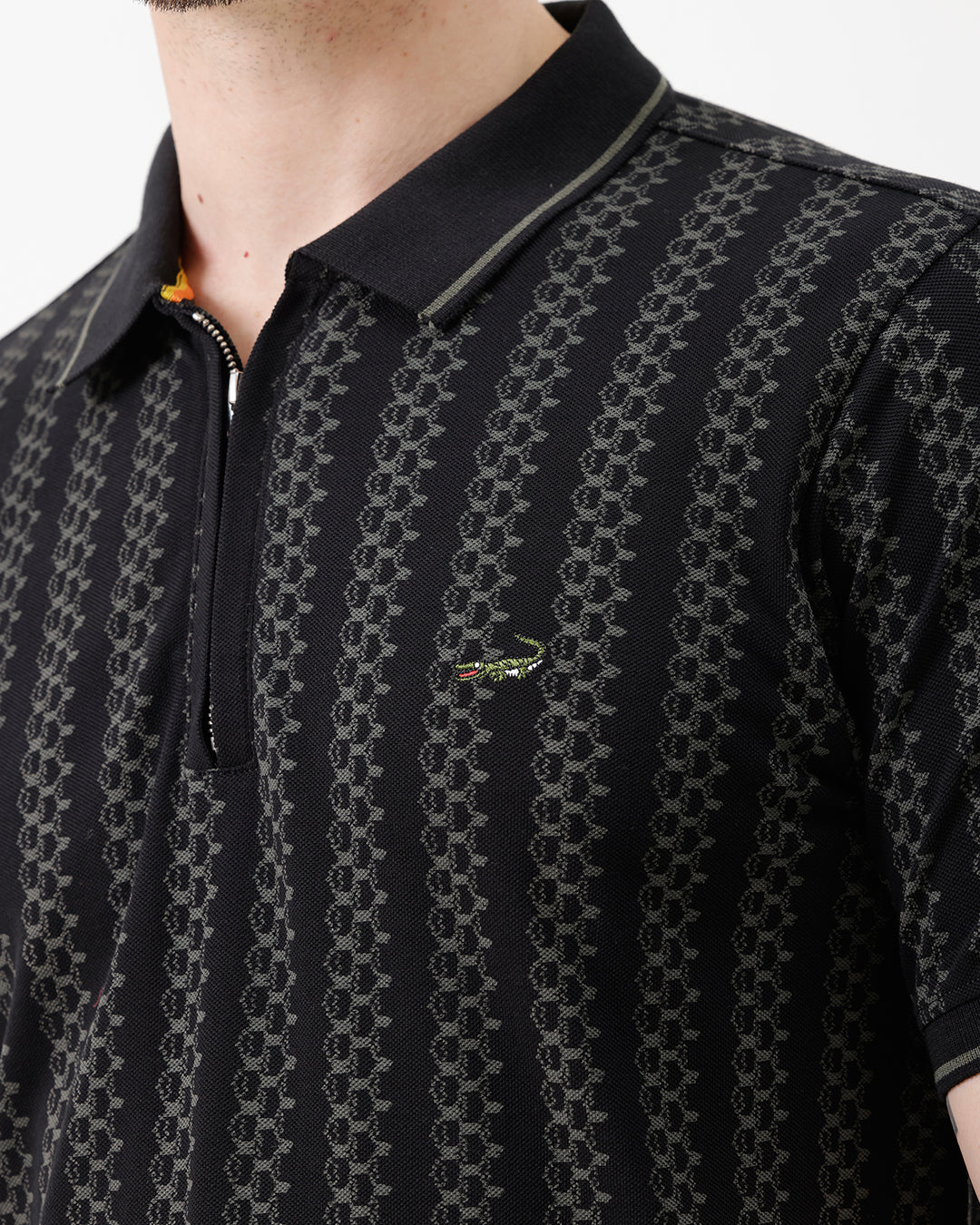 A man wearing a black short-sleeve polo shirt with a subtle geometric pattern, paired with dark gray trousers, standing against a plain white studio background.