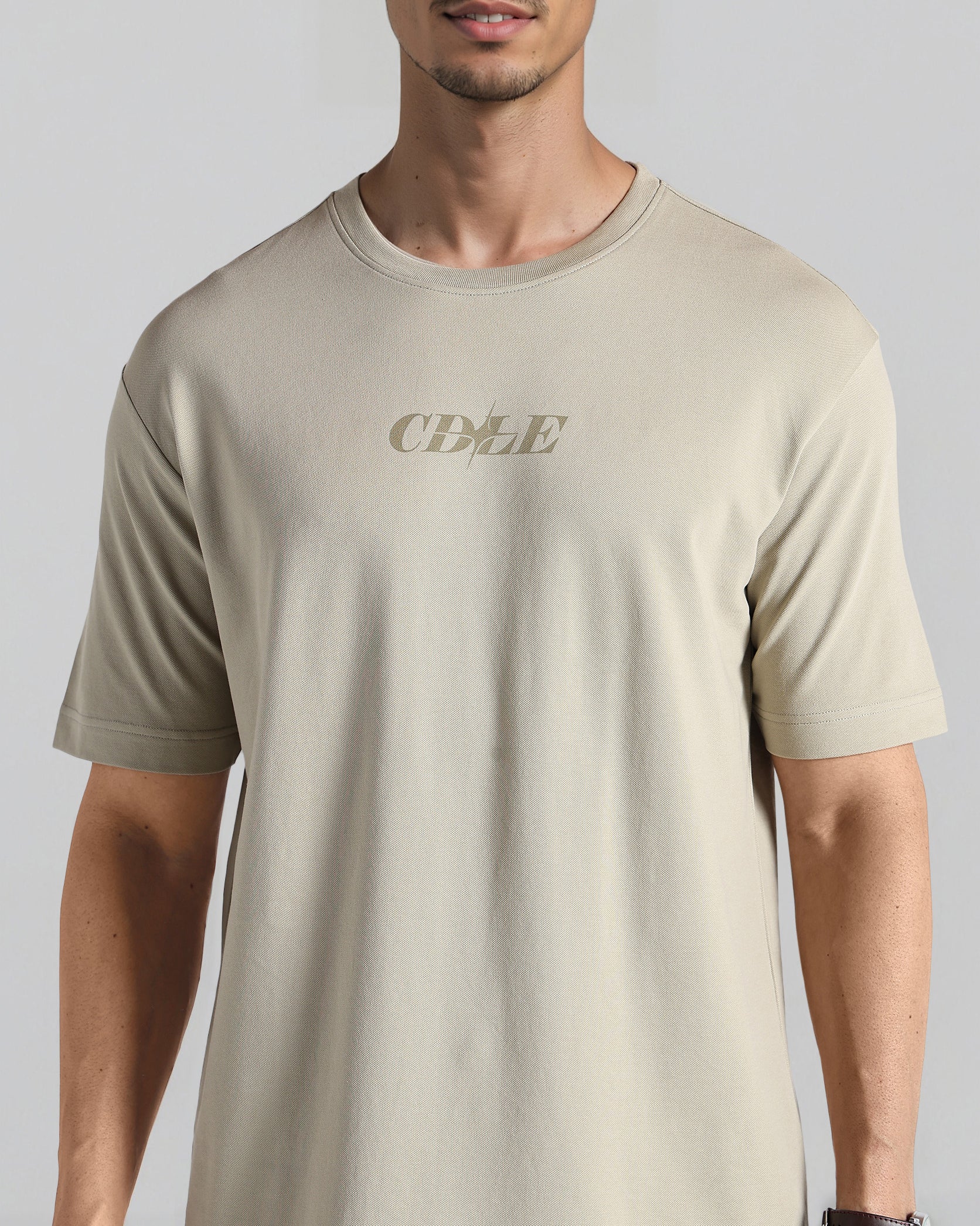 Man wearing a beige t-shirt with 'CDLE' logo on a gray background