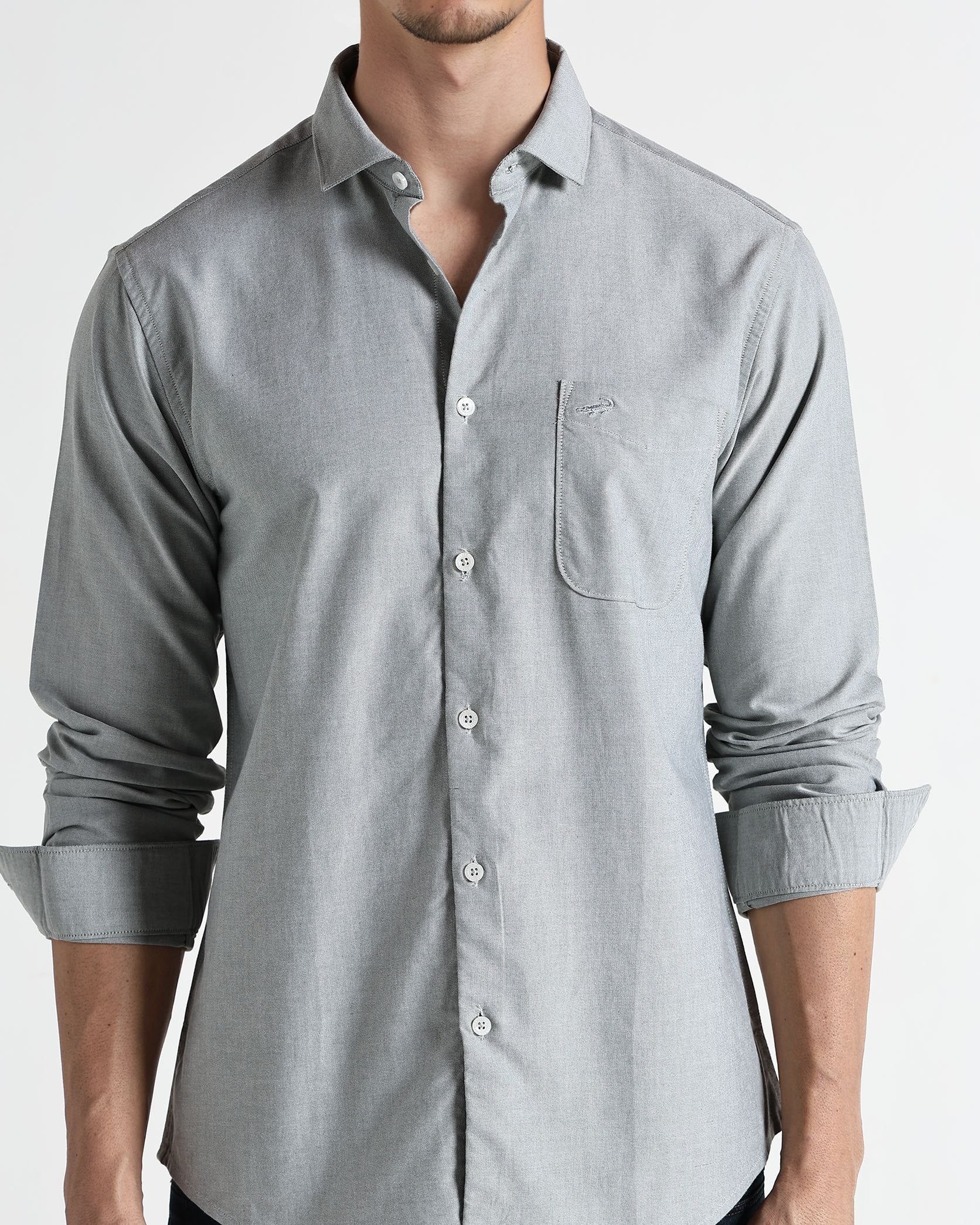 Man wearing a light gray button-up shirt with rolled-up sleeves on a white background