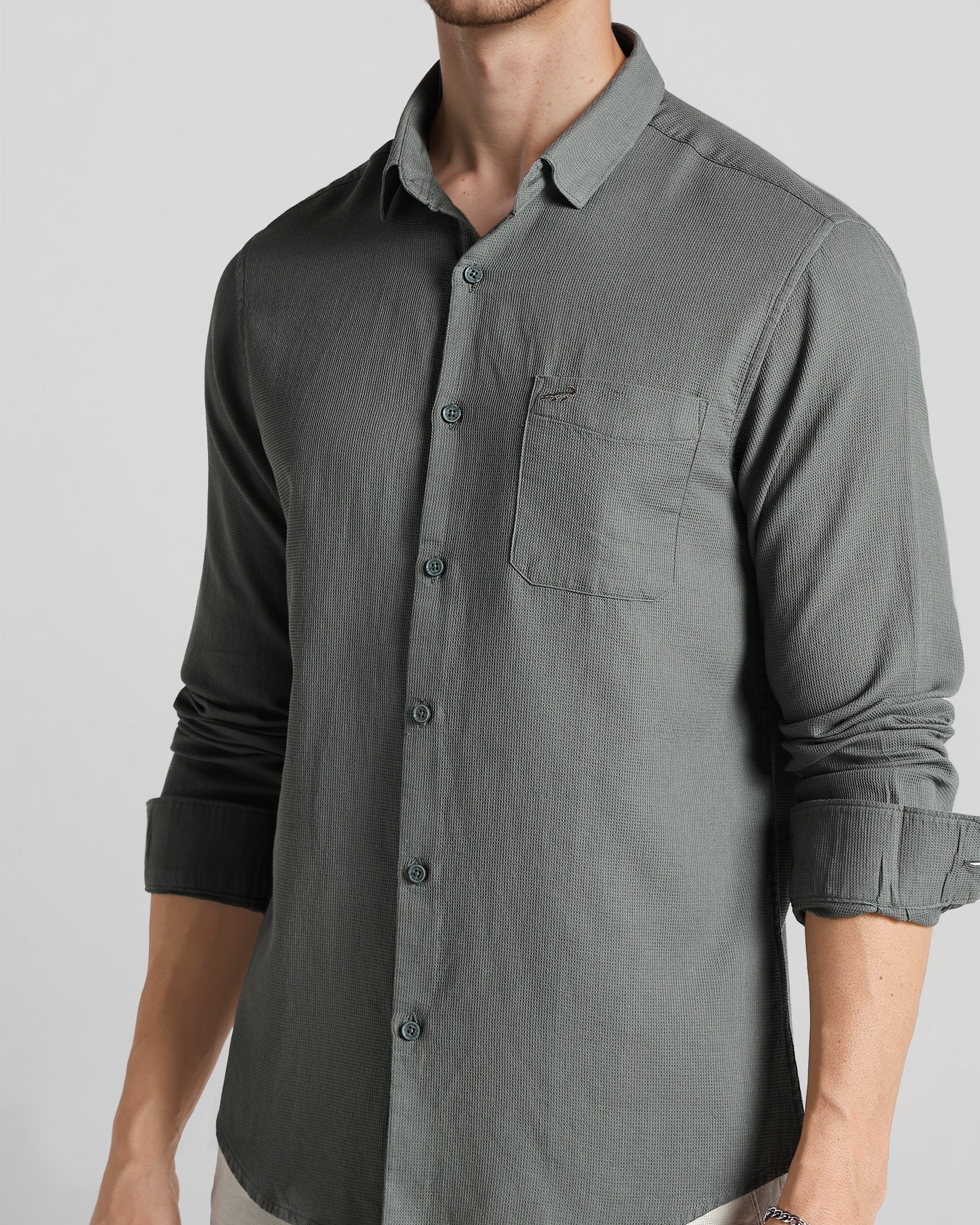 Man wearing a gray button-up shirt with rolled-up sleeves on a plain background