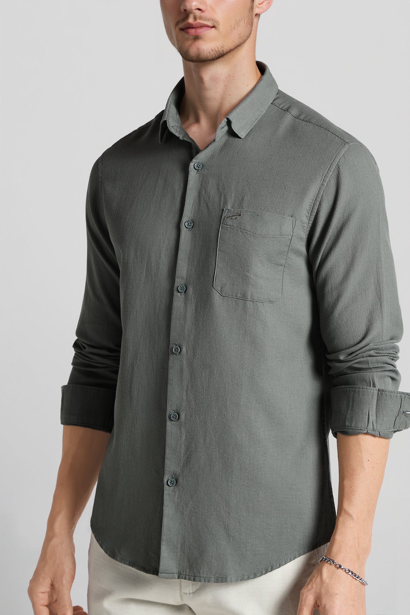 Man wearing a gray button-up shirt with rolled-up sleeves on a plain background