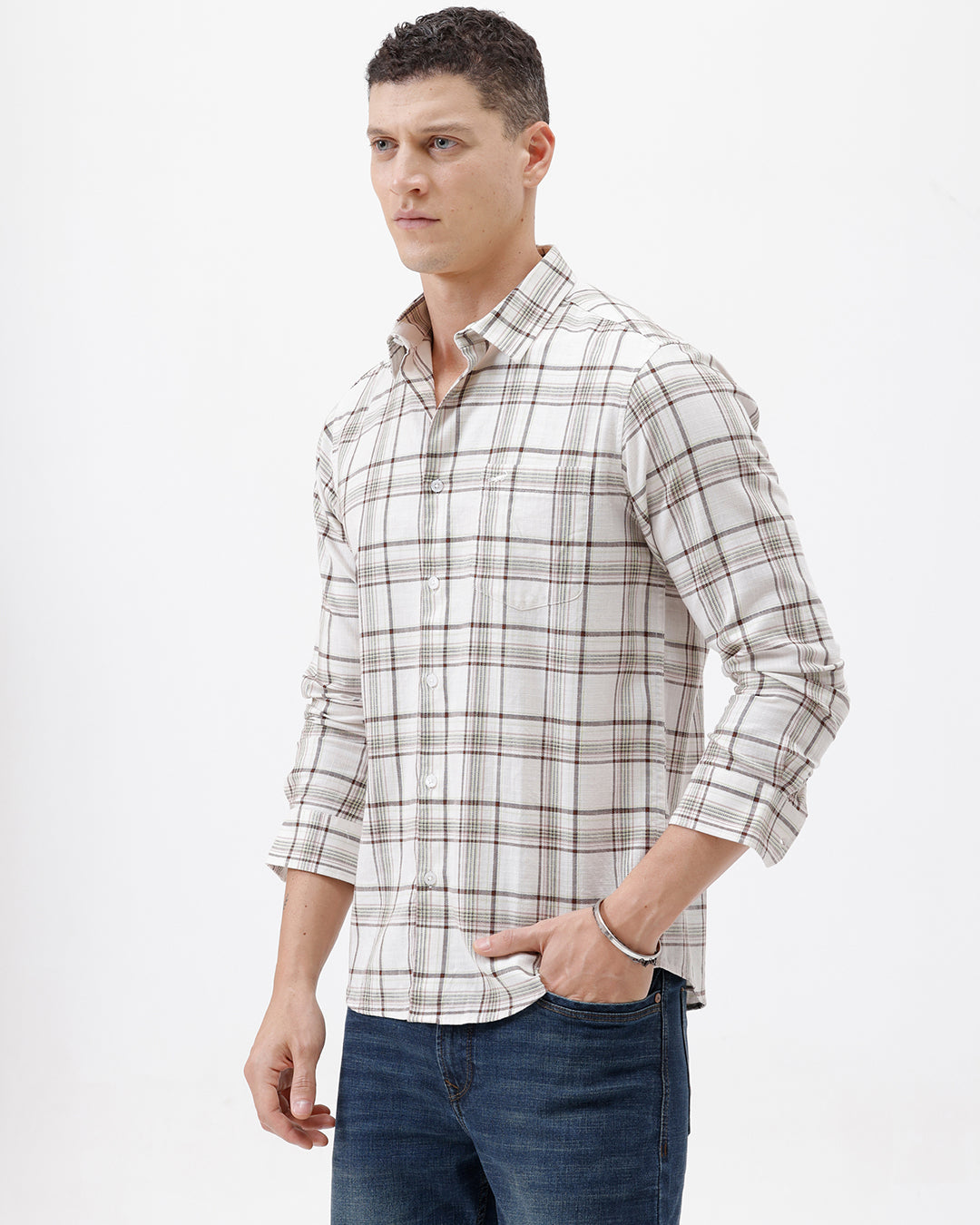 A man wearing a long-sleeve plaid button-up shirt in beige and brown with dark blue jeans, standing against a plain white studio background.