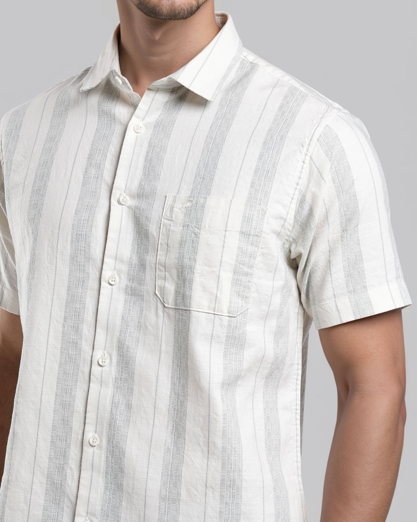 Man wearing a white and gray striped short-sleeve shirt against a gray background