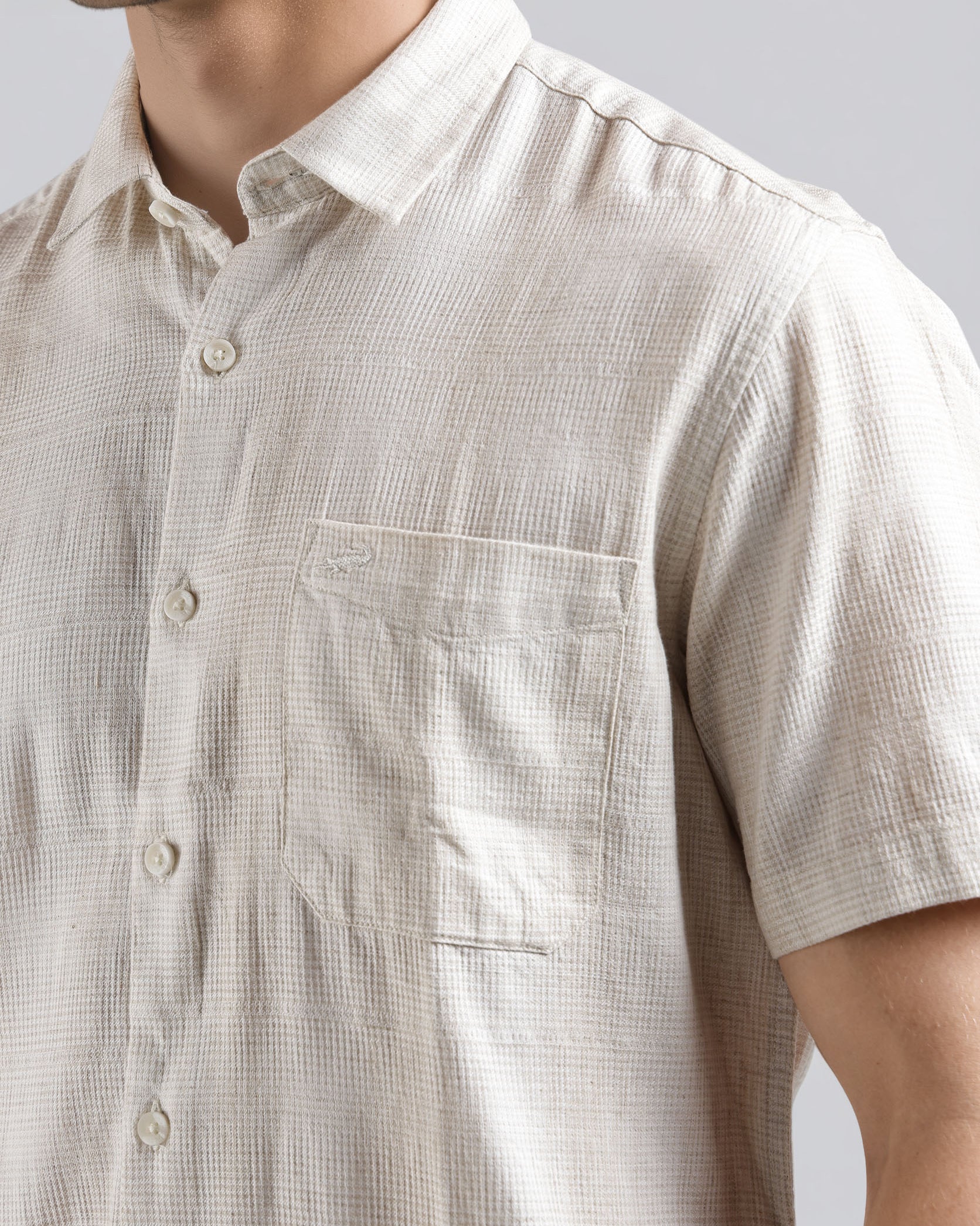 Close-up of a person wearing a beige checkered shirt with a plain background