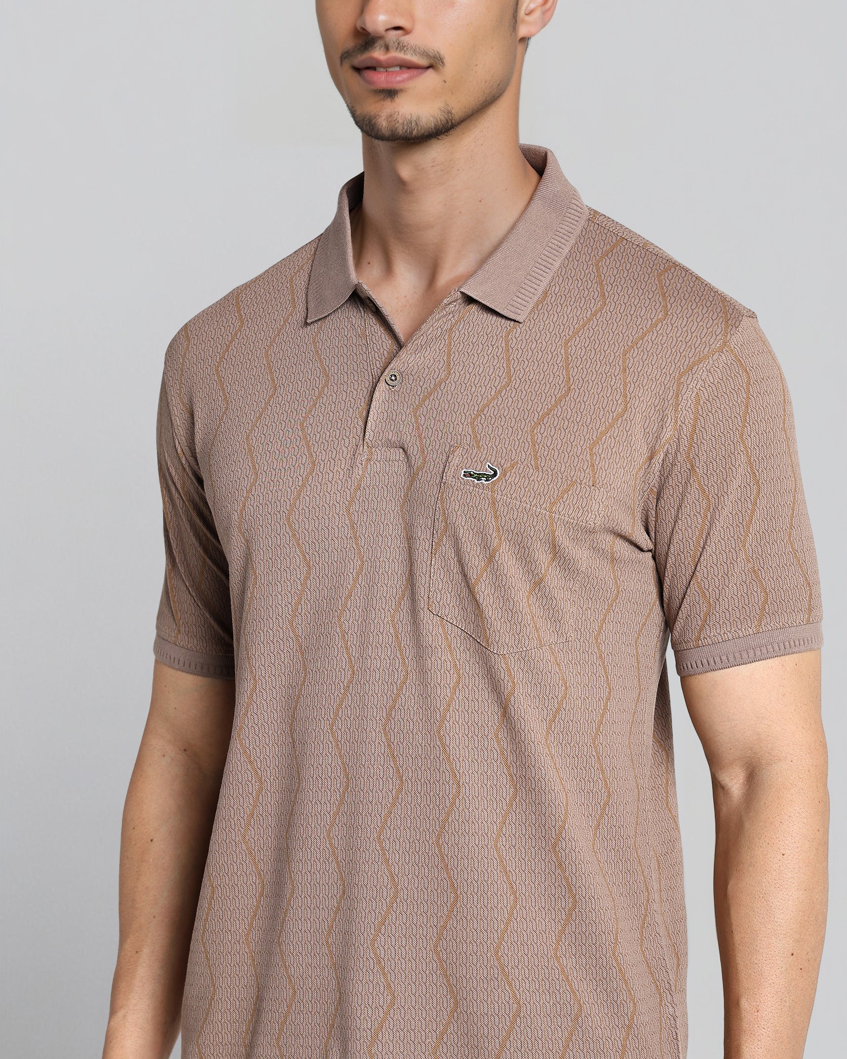 Man wearing a brown patterned polo shirt against a gray background