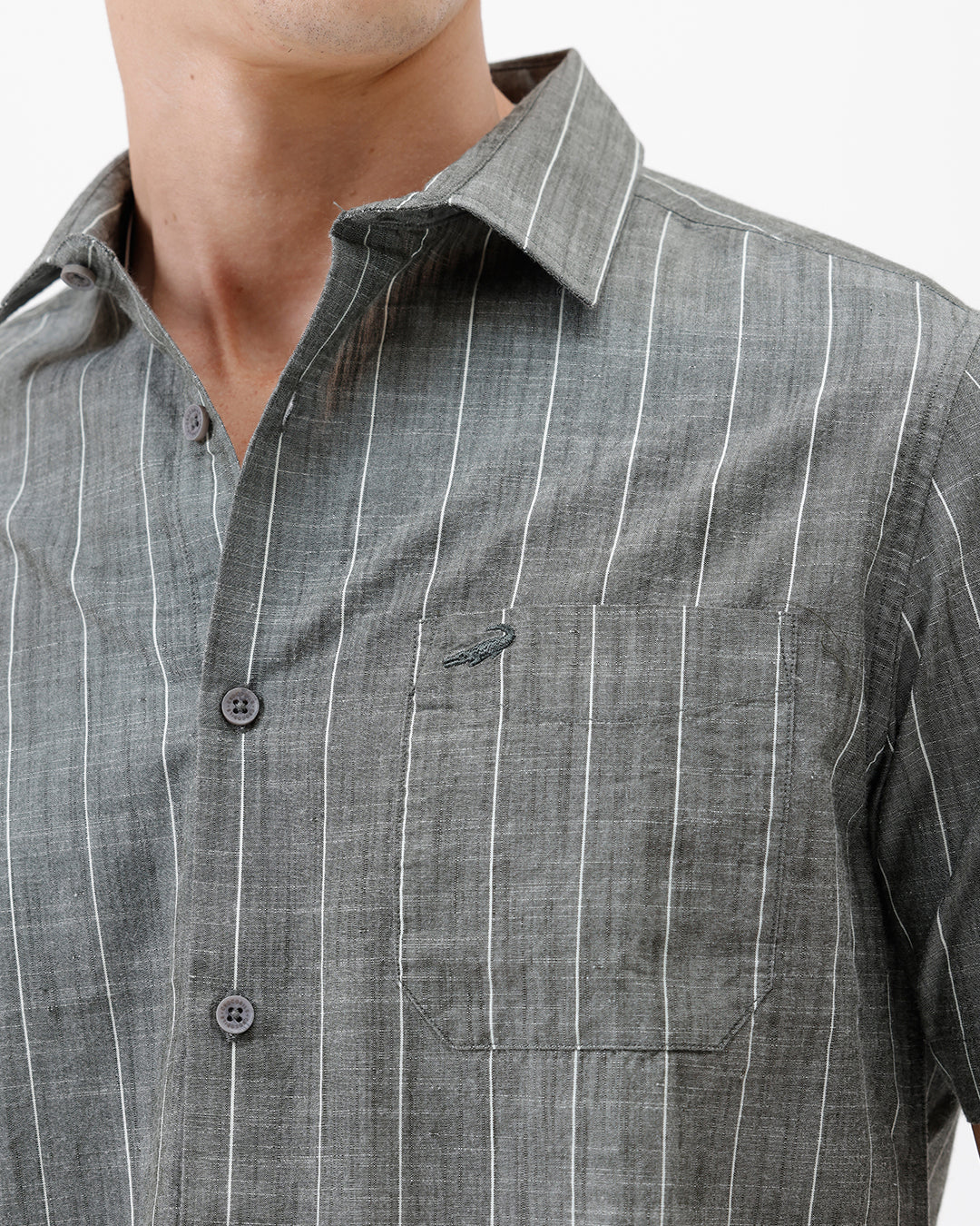 A man wearing a short-sleeve button-up shirt with a gray and white vertical stripe pattern, paired with black pants, standing against a plain white studio background.