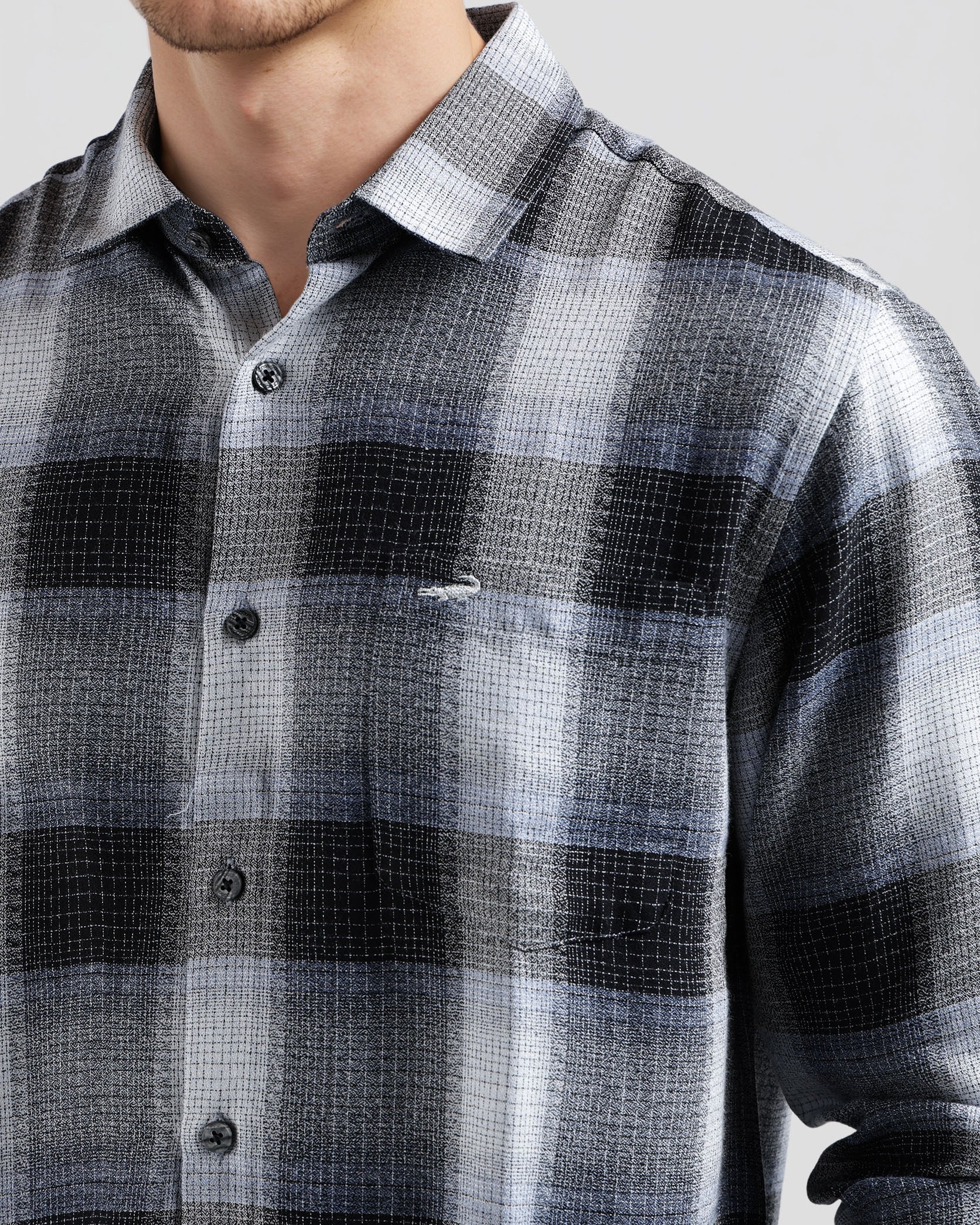 Man wearing a plaid shirt with a visible brand logo on a light gray background
