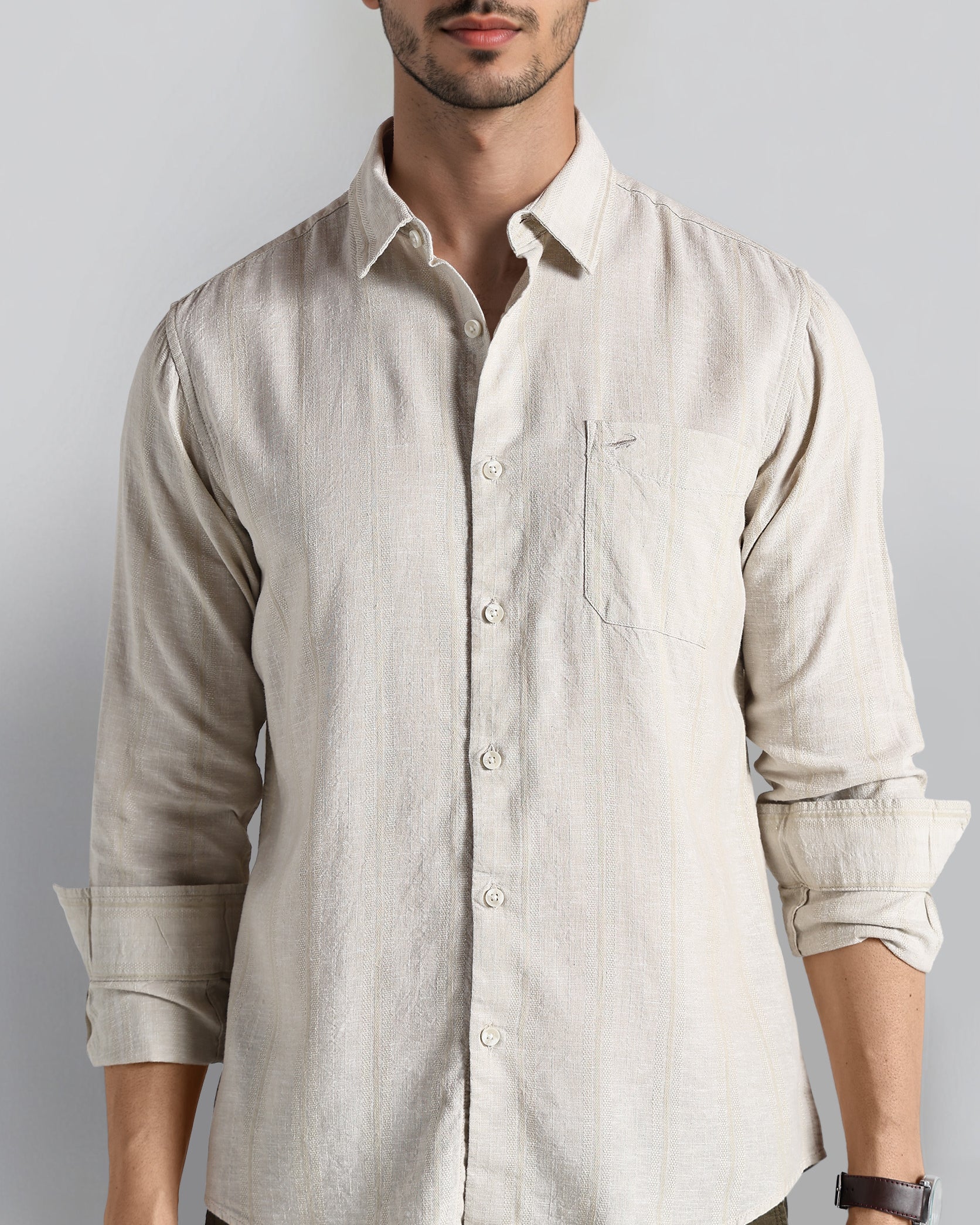 Man wearing a beige button-up shirt with rolled-up sleeves against a plain background