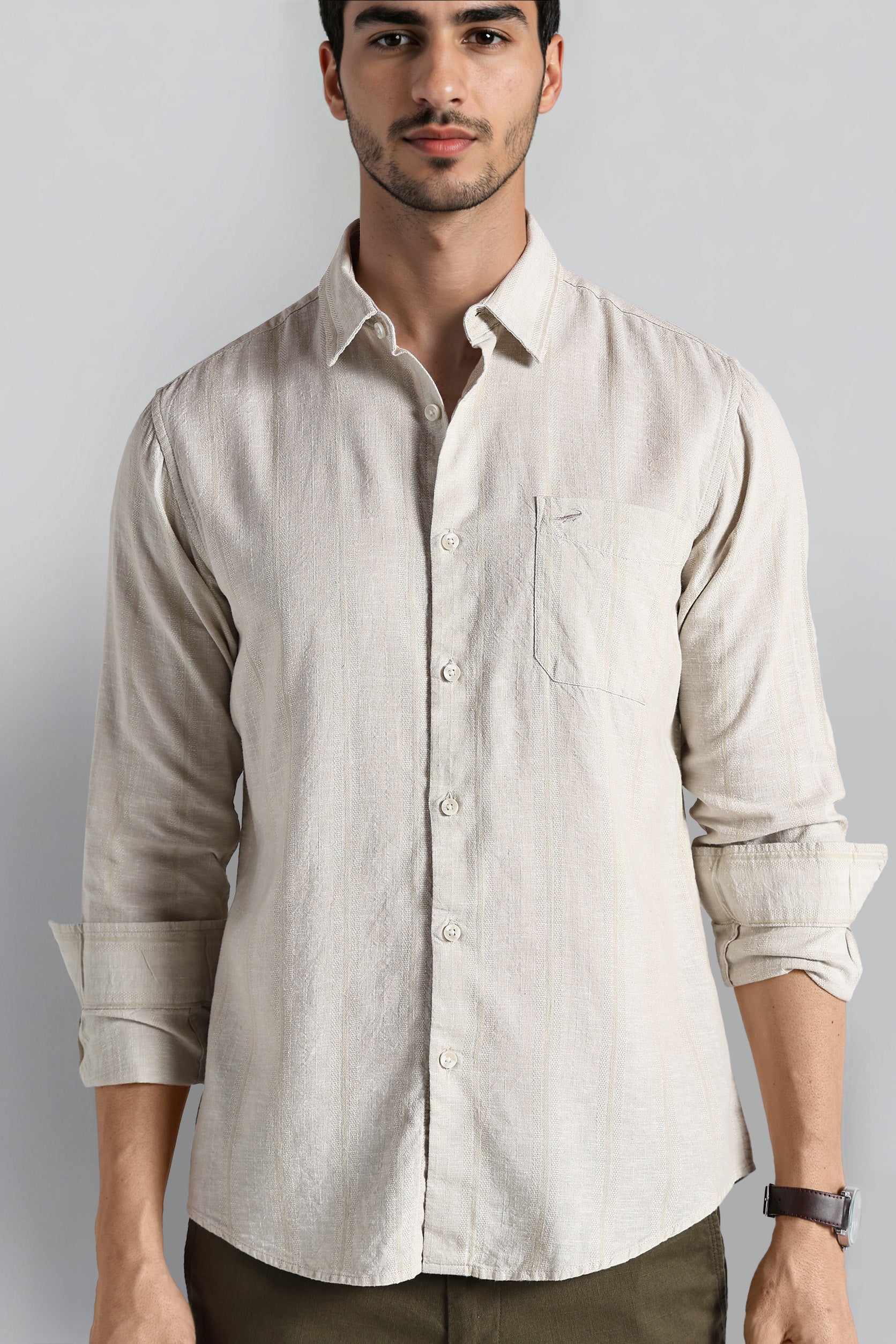 Man wearing a beige button-up shirt with rolled-up sleeves against a plain background