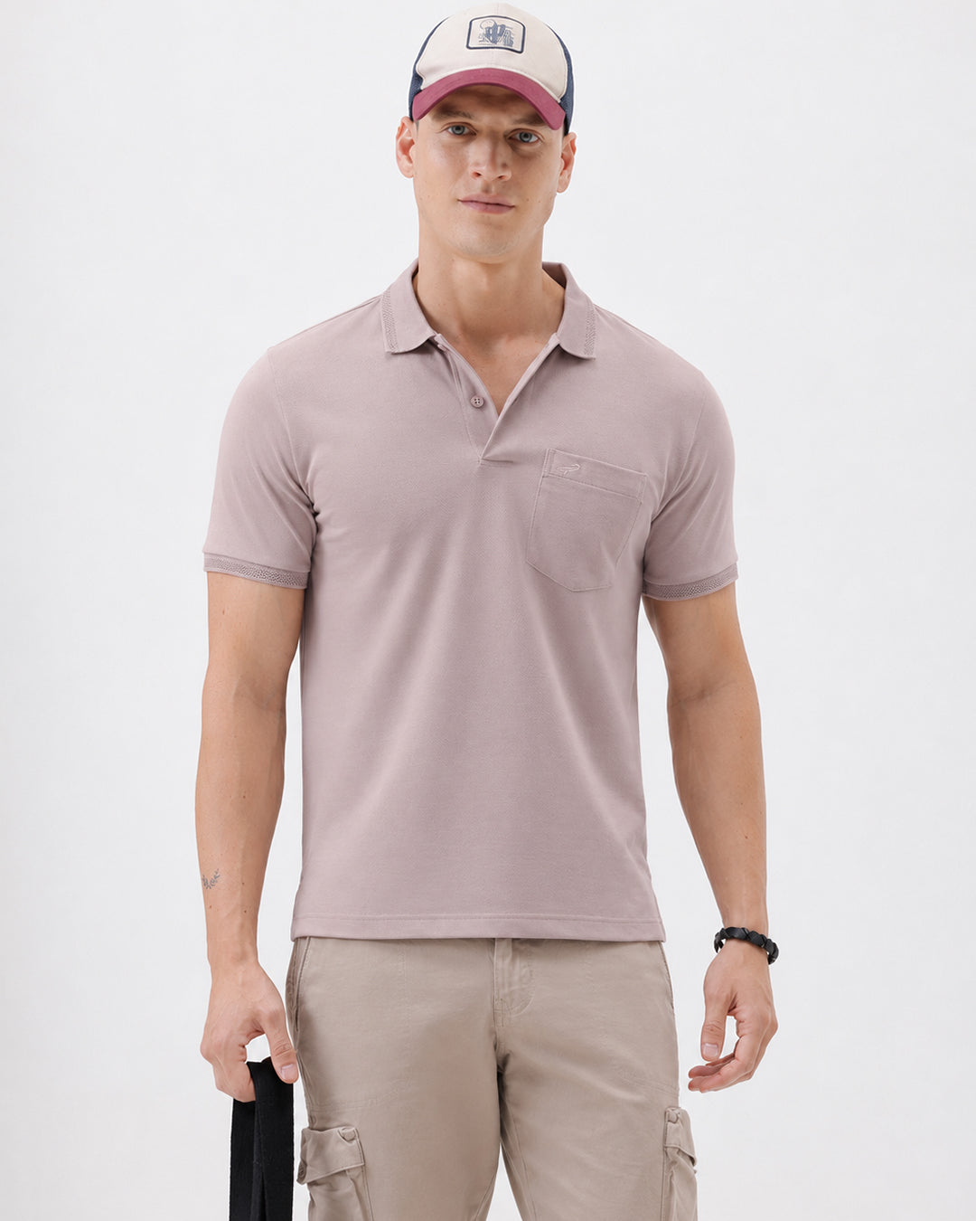 A man modeling a short-sleeve polo shirt in a dusty mauve-pink color, paired with khaki cargo pants and a baseball cap, against a plain light gray background.