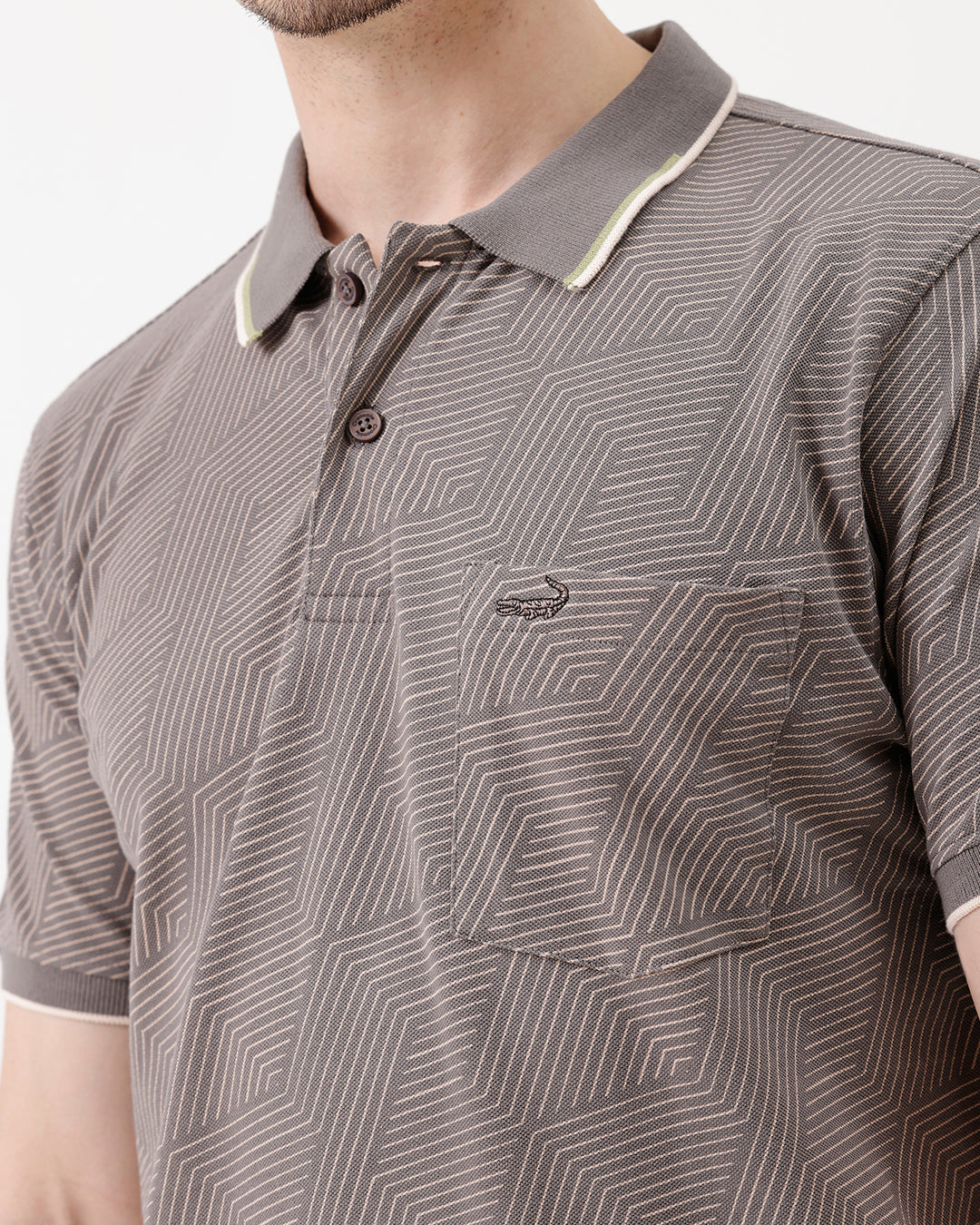 A man wearing a short-sleeve polo shirt with a gray and white geometric pattern, paired with beige trousers, standing against a plain white studio background.