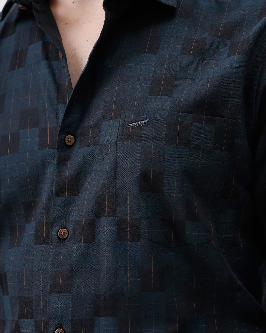 A man wearing a dark navy blue patterned long-sleeve button-up shirt and black trousers, standing against a plain white studio background.