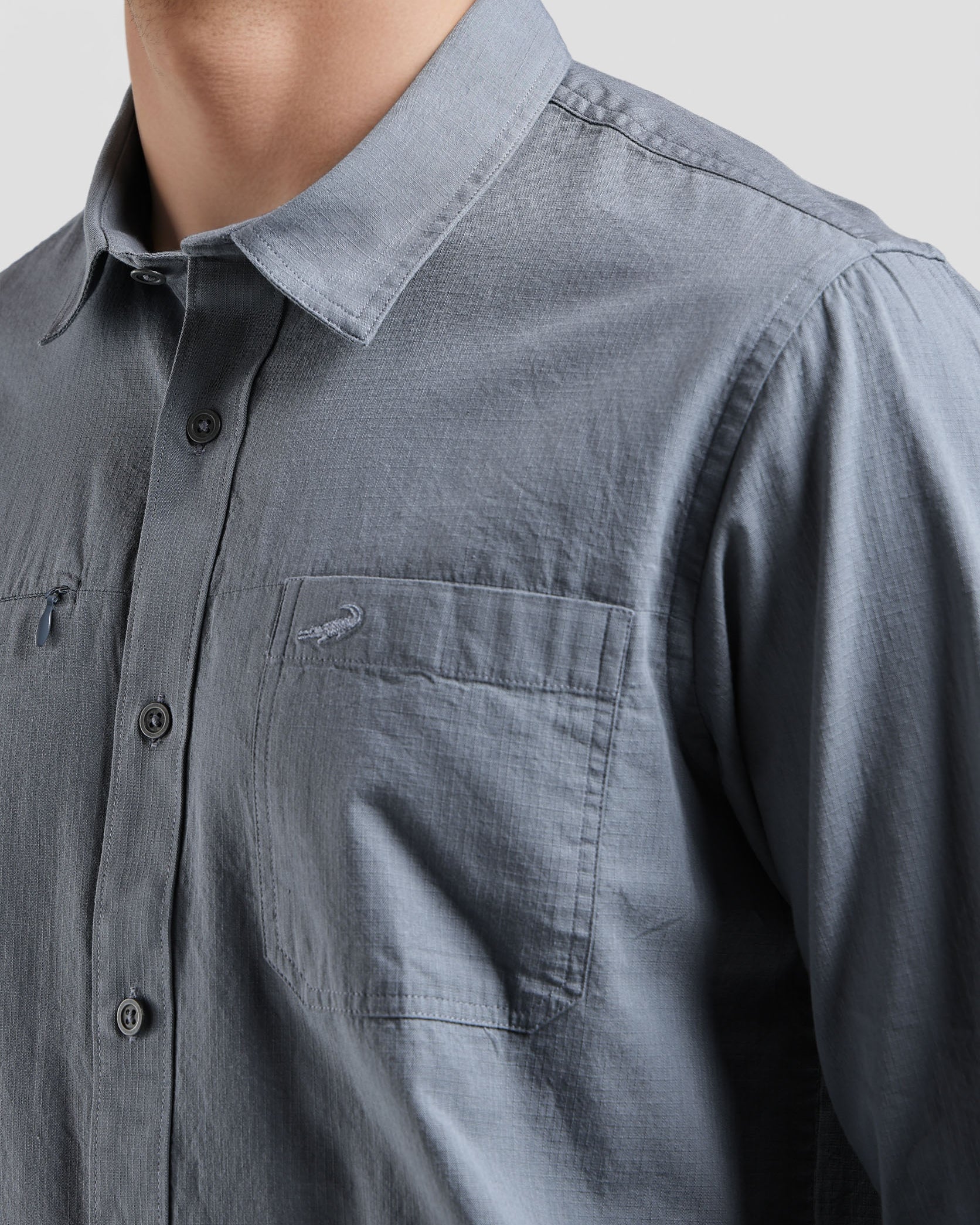 Close-up of a person wearing a gray button-up shirt with a collar and pocket.