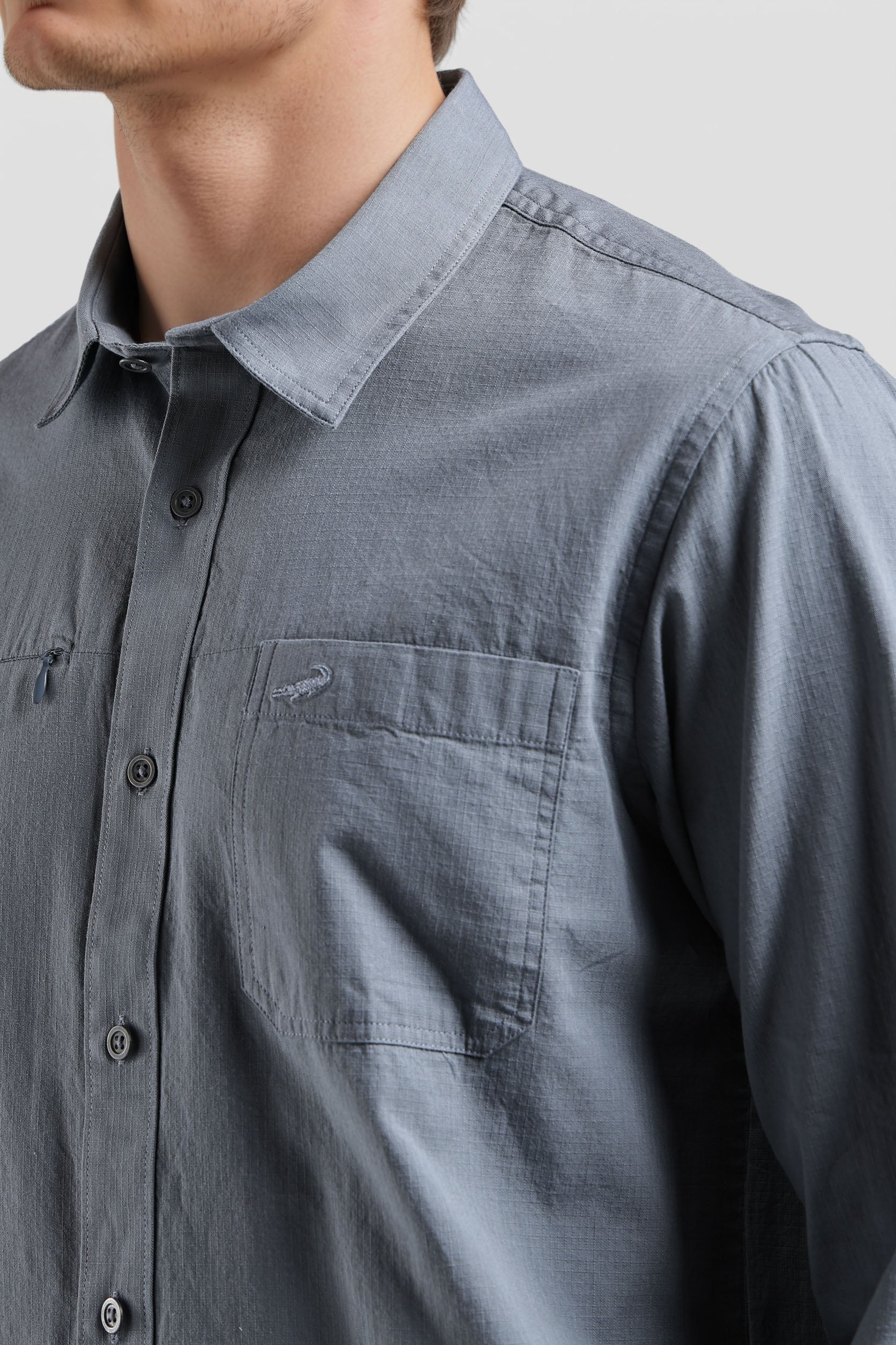 Close-up of a person wearing a gray button-up shirt with a collar and pocket.