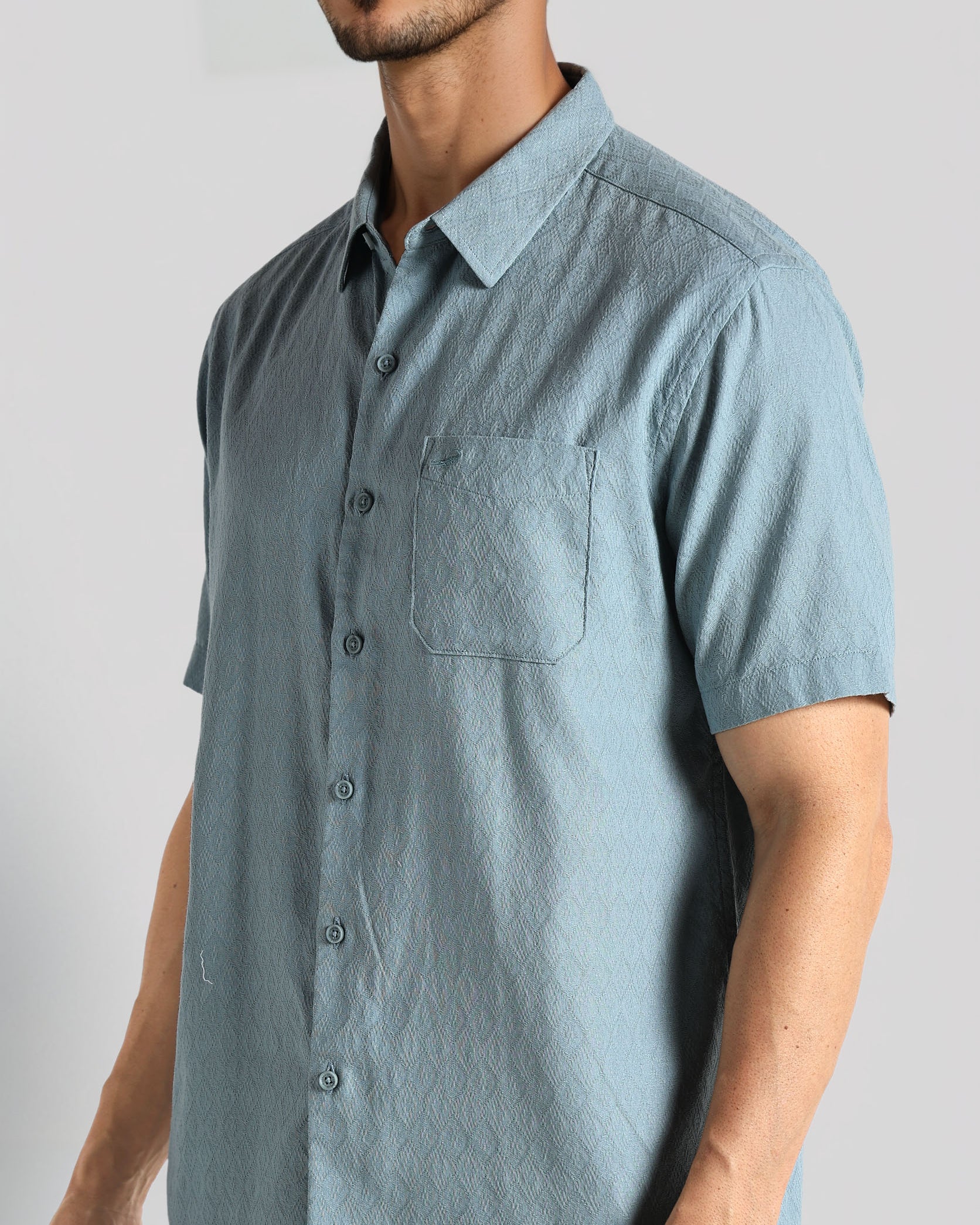 Man wearing a light blue short-sleeve button-up shirt against a plain background