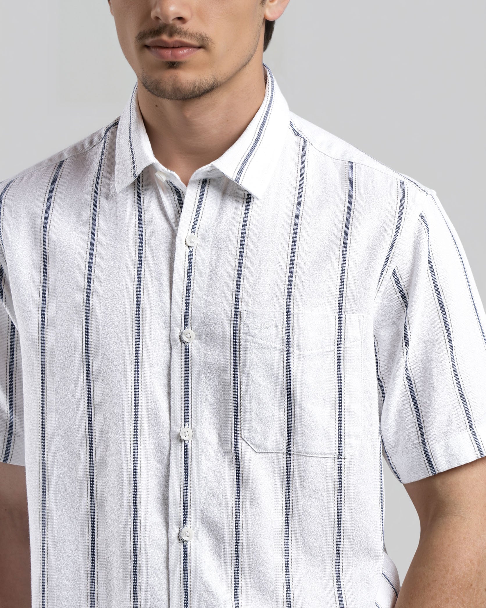 Man wearing a white short-sleeve shirt with blue stripes against a gray background
