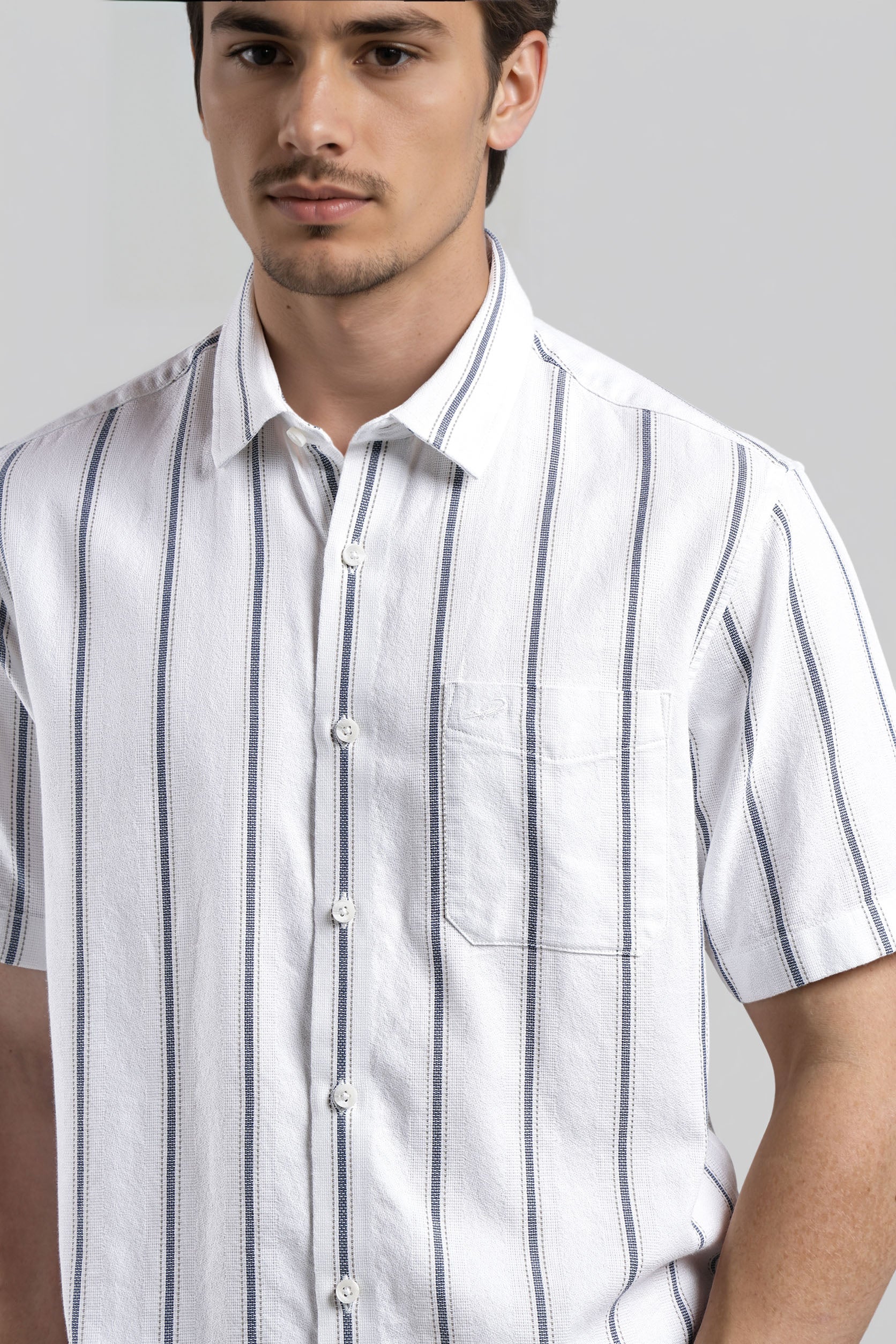 Man wearing a white short-sleeve shirt with blue stripes against a gray background