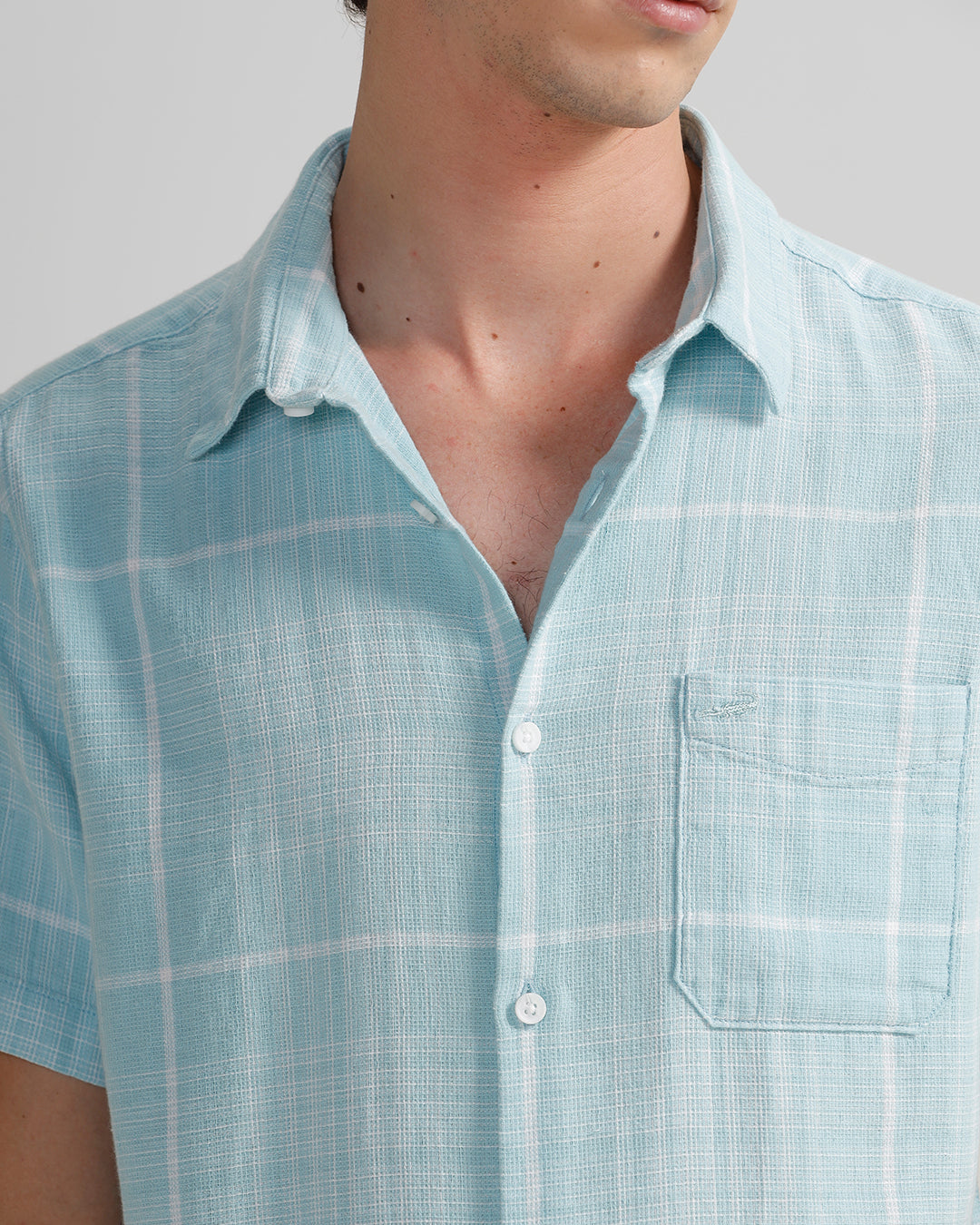 A man wearing a blue short-sleeved checkered shirt with a collar and a pocket on the chest.