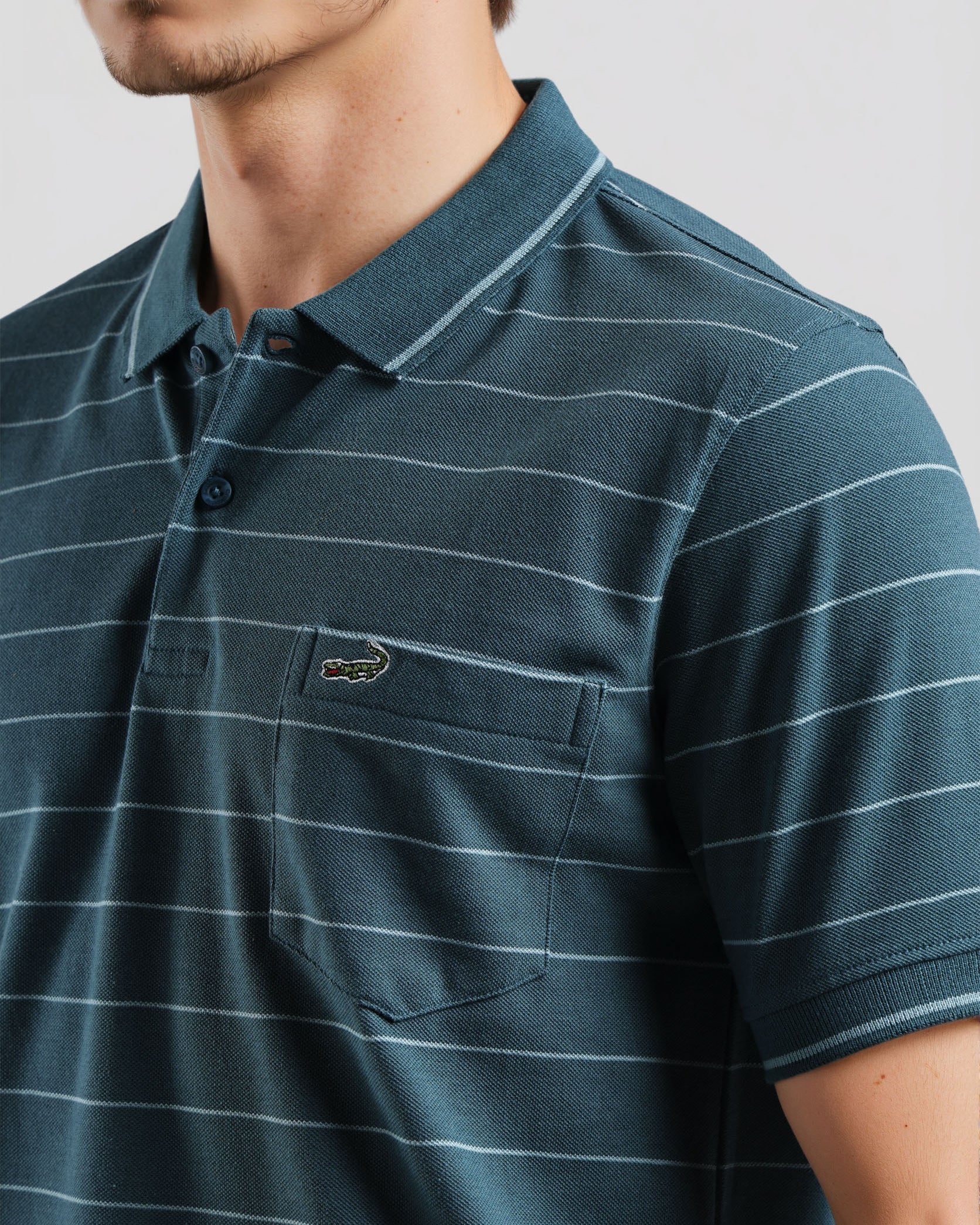 Man wearing a green striped polo shirt with a brand logo on a light gray background