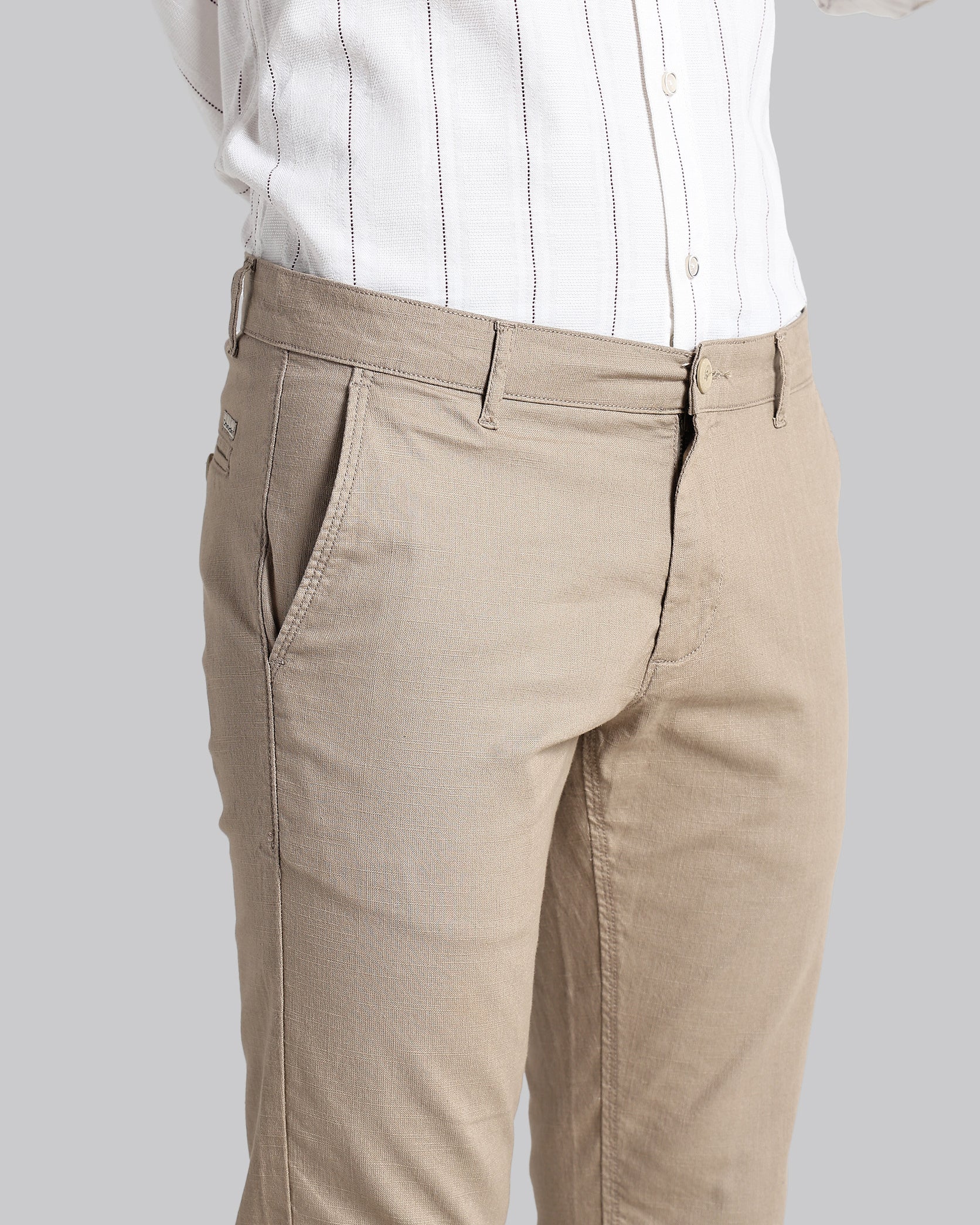 Beige pants worn with a white shirt on a plain background
