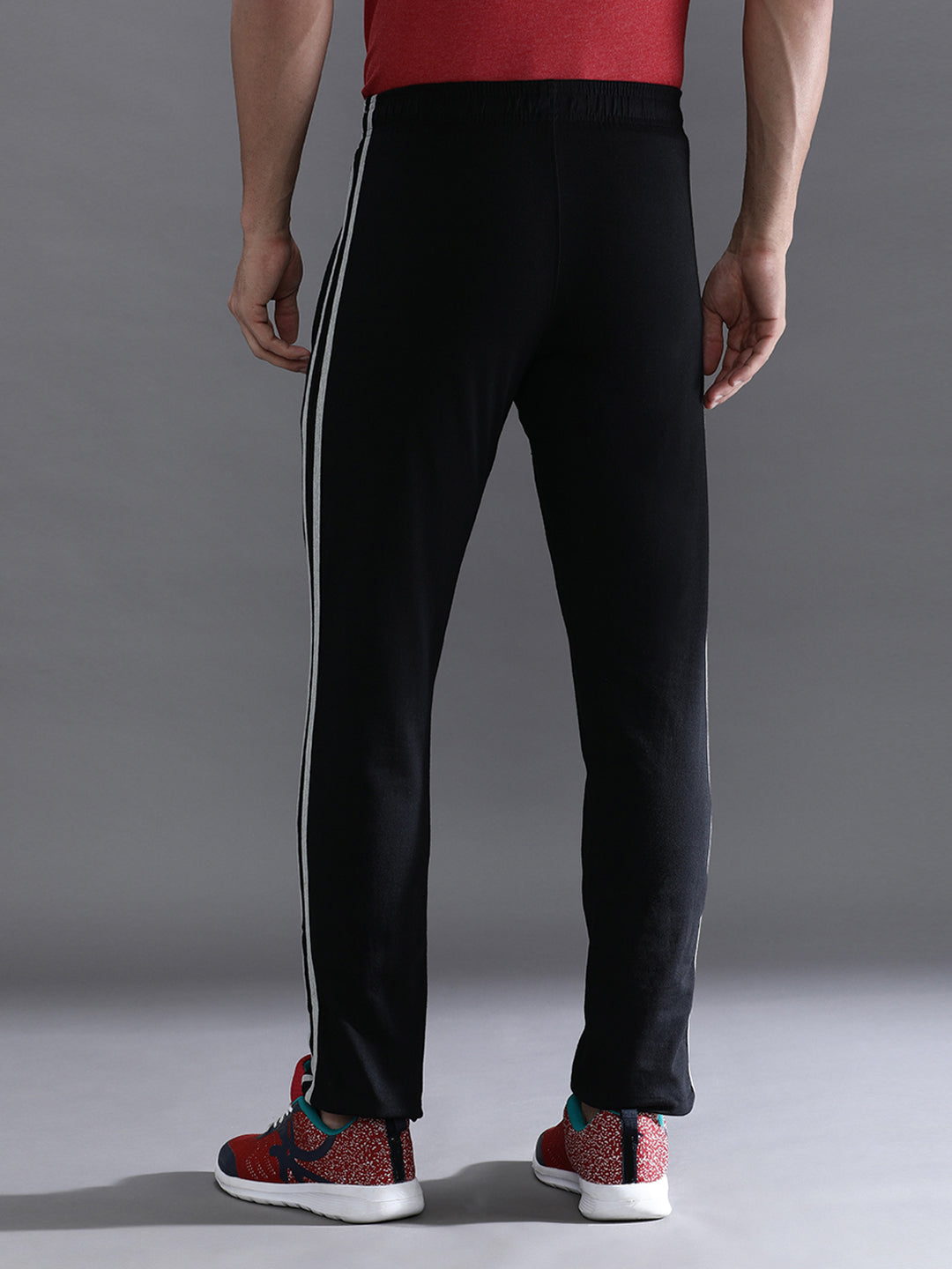 Person wearing black track pants with white stripes on a gray background